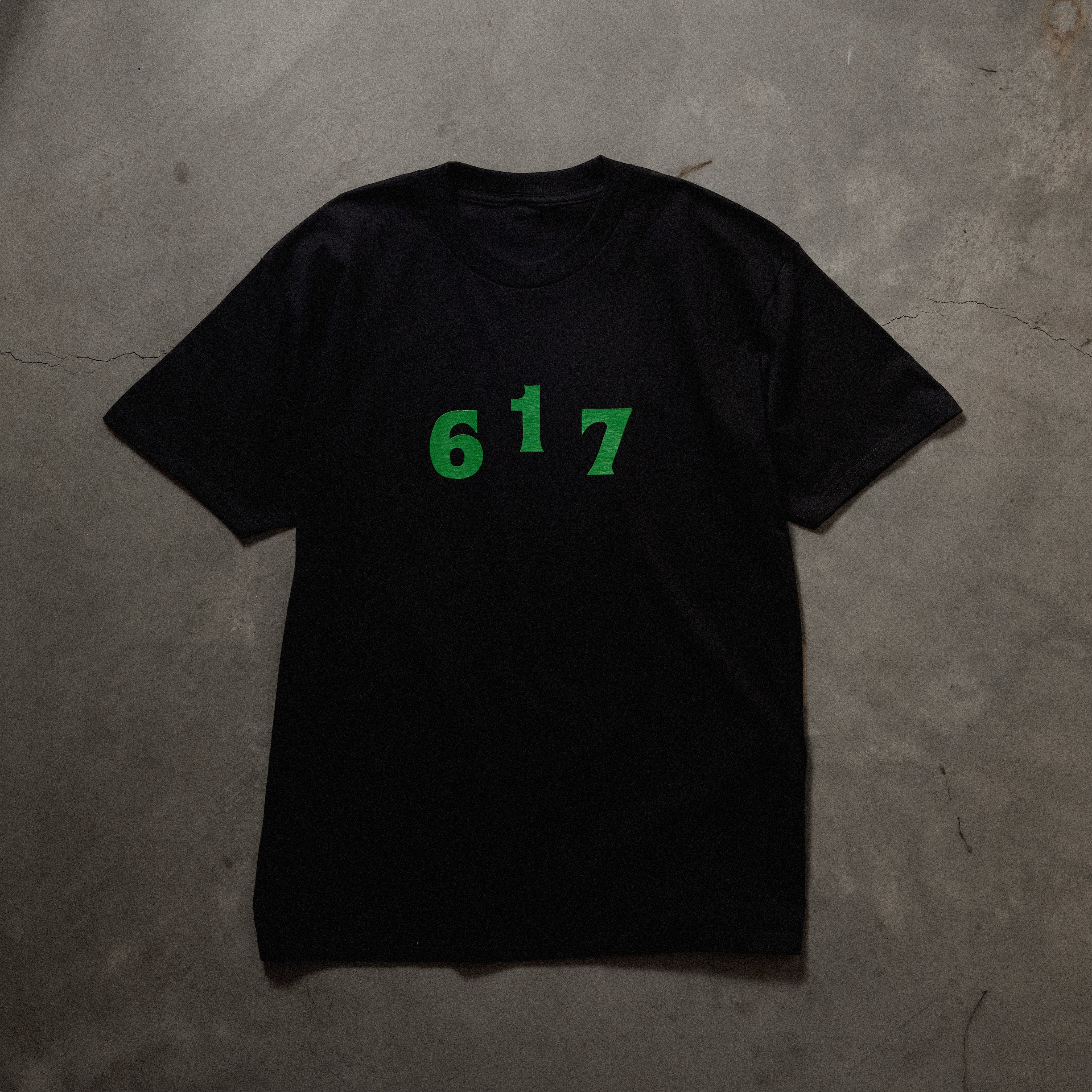 Full front image of black tee with green printed 617 area code font on chest