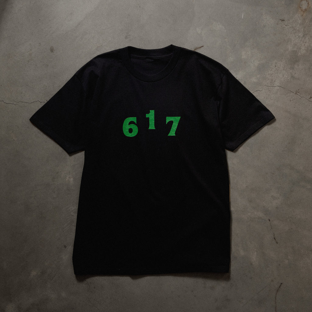 Full front image of black tee with green printed 617 area code font on chest