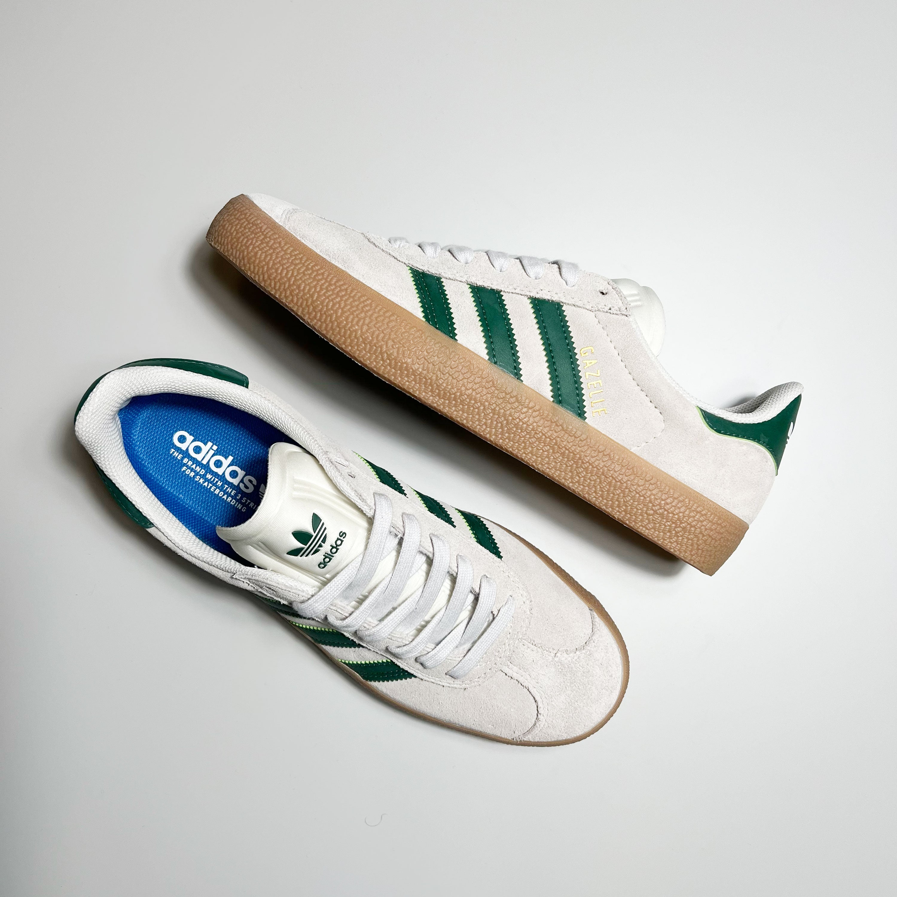 TOP AND SIDE VIEW ADIDAS GAZELLE ADV IN CRYSTAL WHITE SUEDE, GREEN LEATHER STRIPES AND HEEL TAB WITH GUM SOLE.
