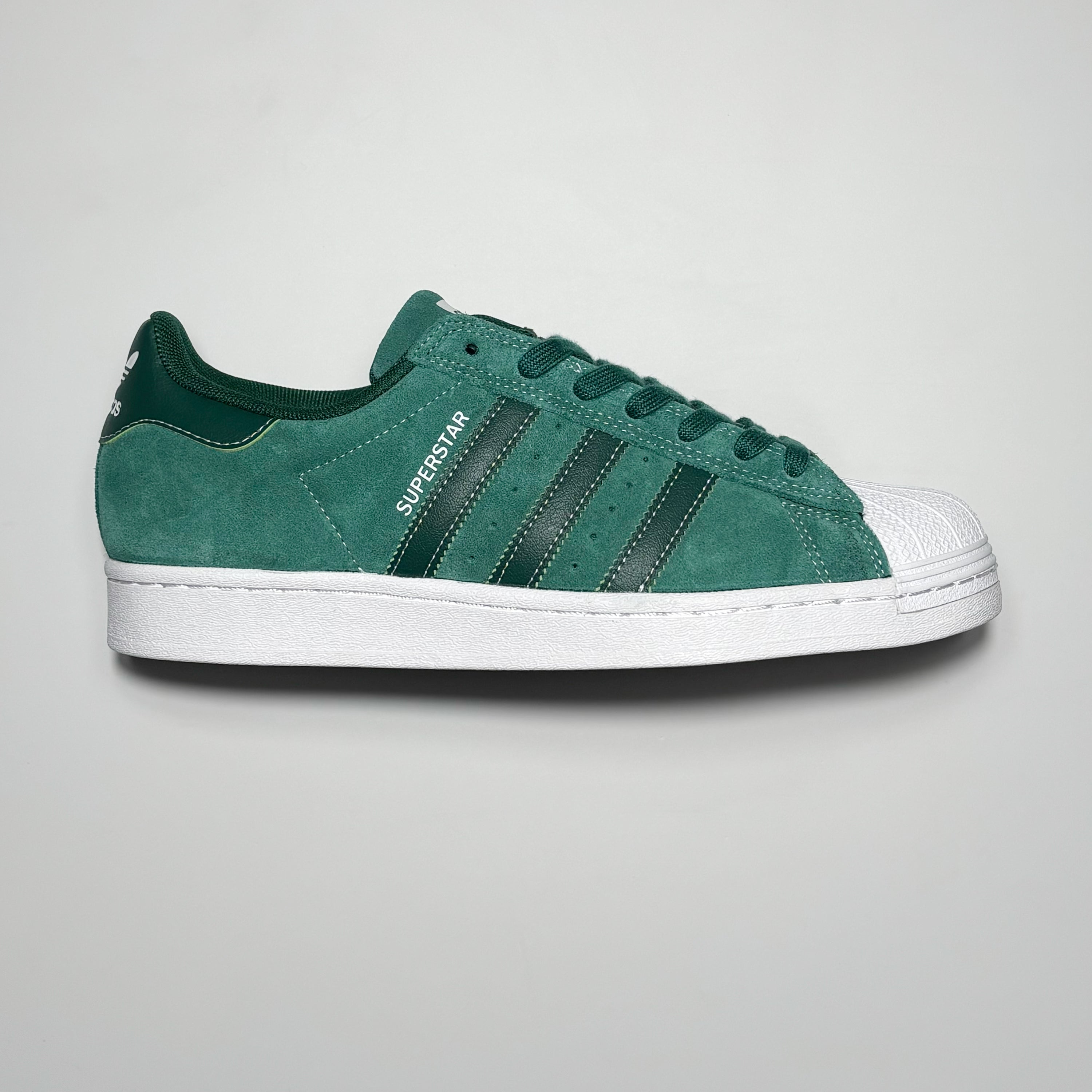 Side image of right shoe.
Green suede with white rubber toe and superstar printed in silver foil on heel panel.