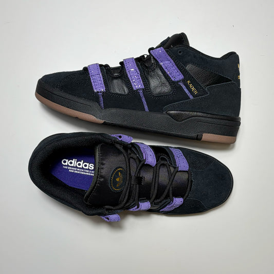 A pair of Adidas Skateboarding Kader Sylla Pro model sneakers in black suede and leather with purple straps and a tan outsole, displayed on a light gray background.