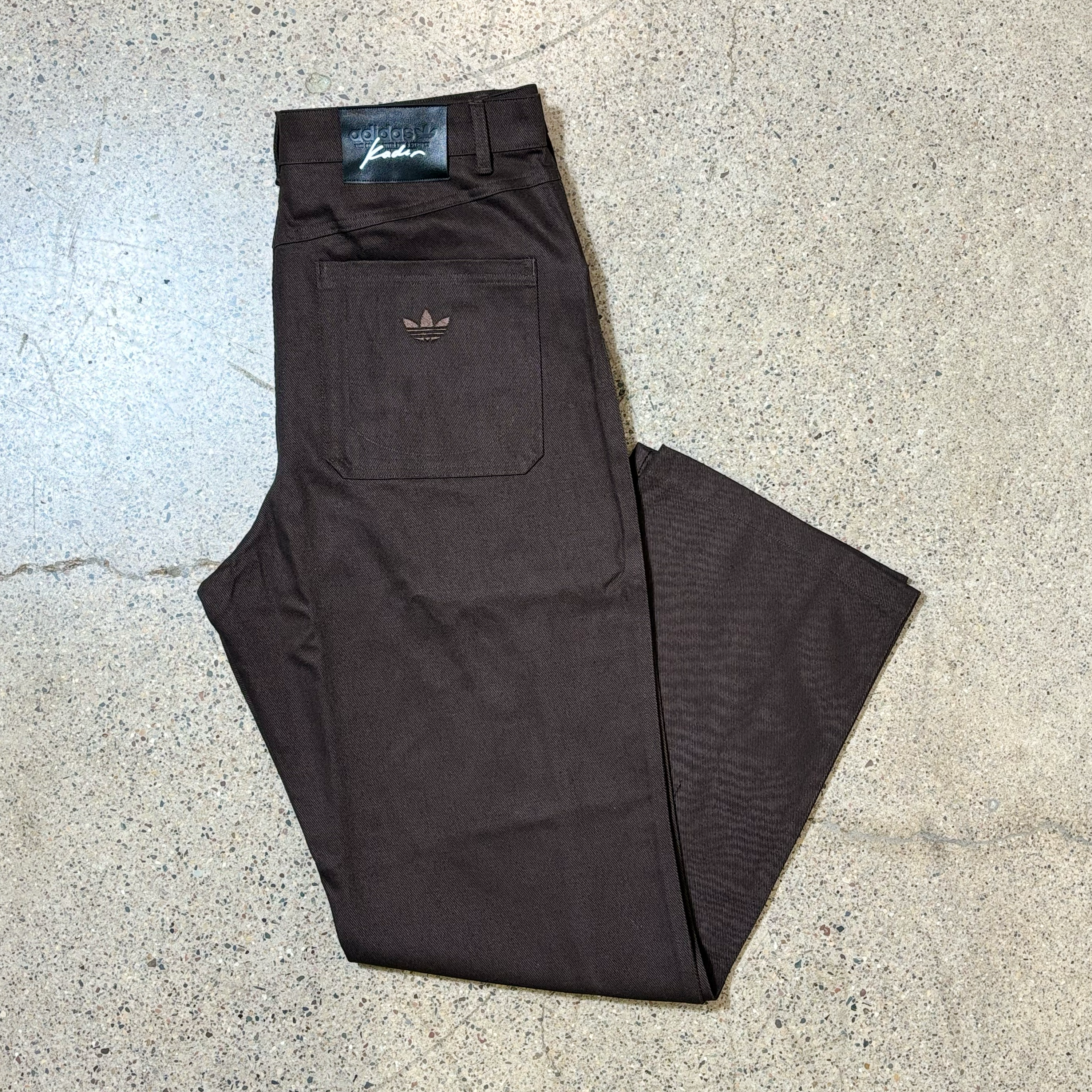 Image of folded brown pant with tonal foil logo embroidered on back pocket.