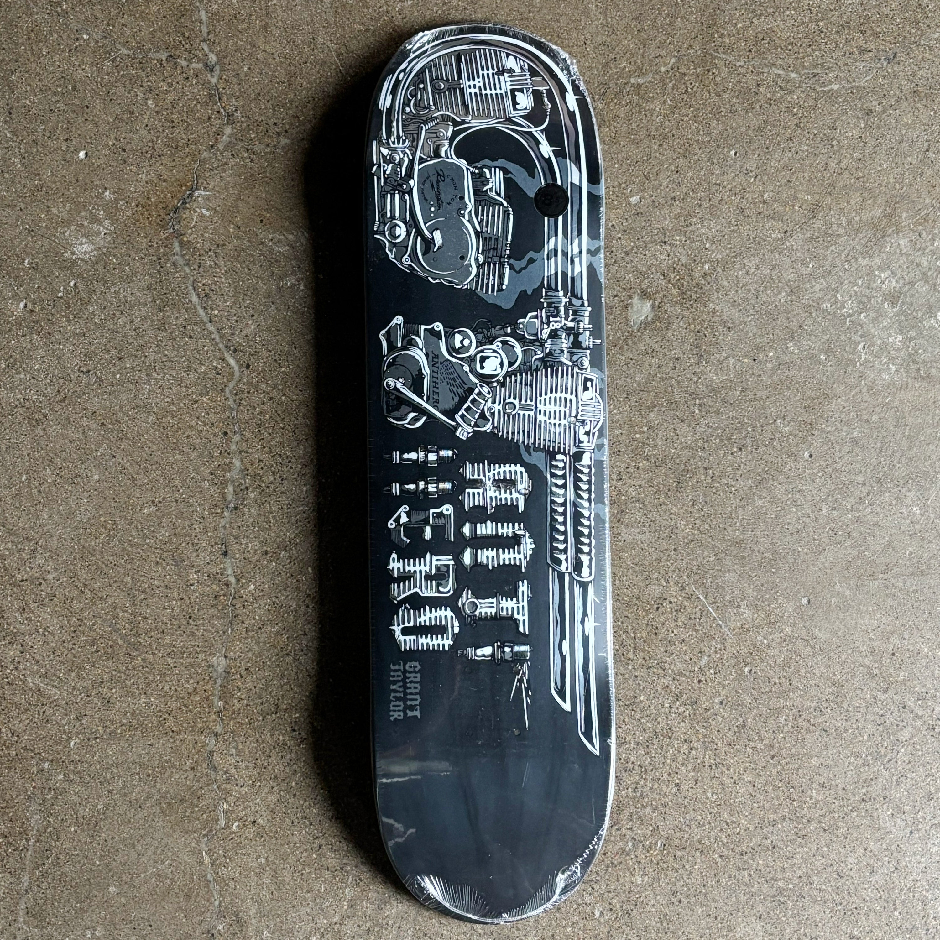 Black skateboard deck with detailed design on a concrete surface