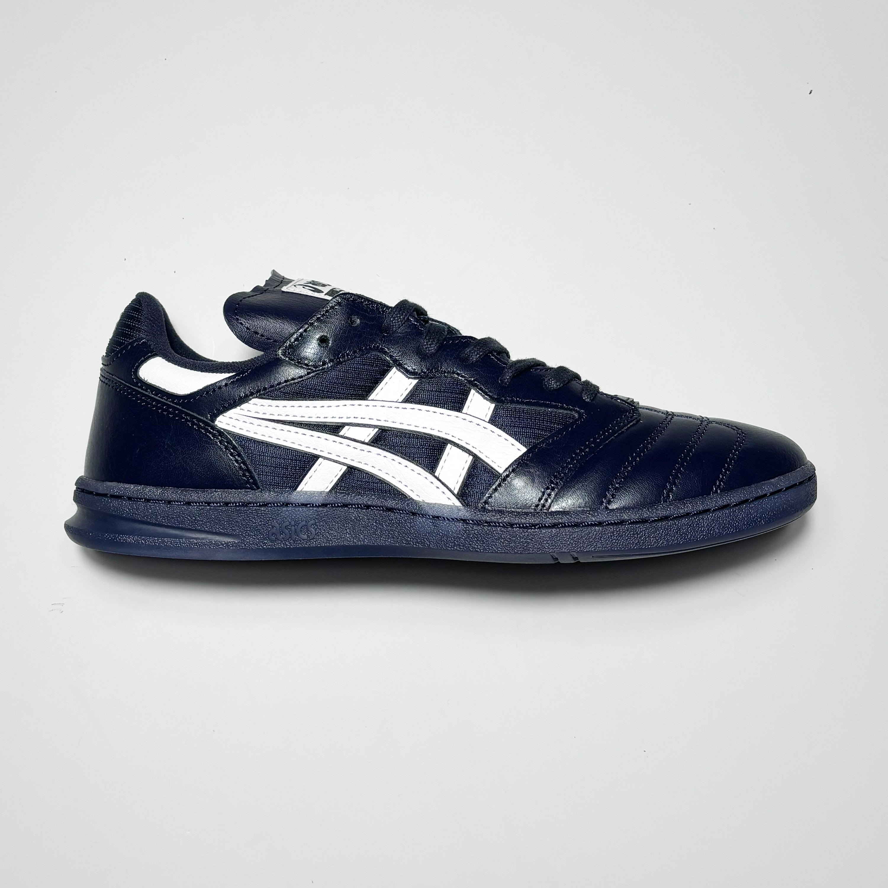 Side image of right shoe. Navy leather with white asics branding.