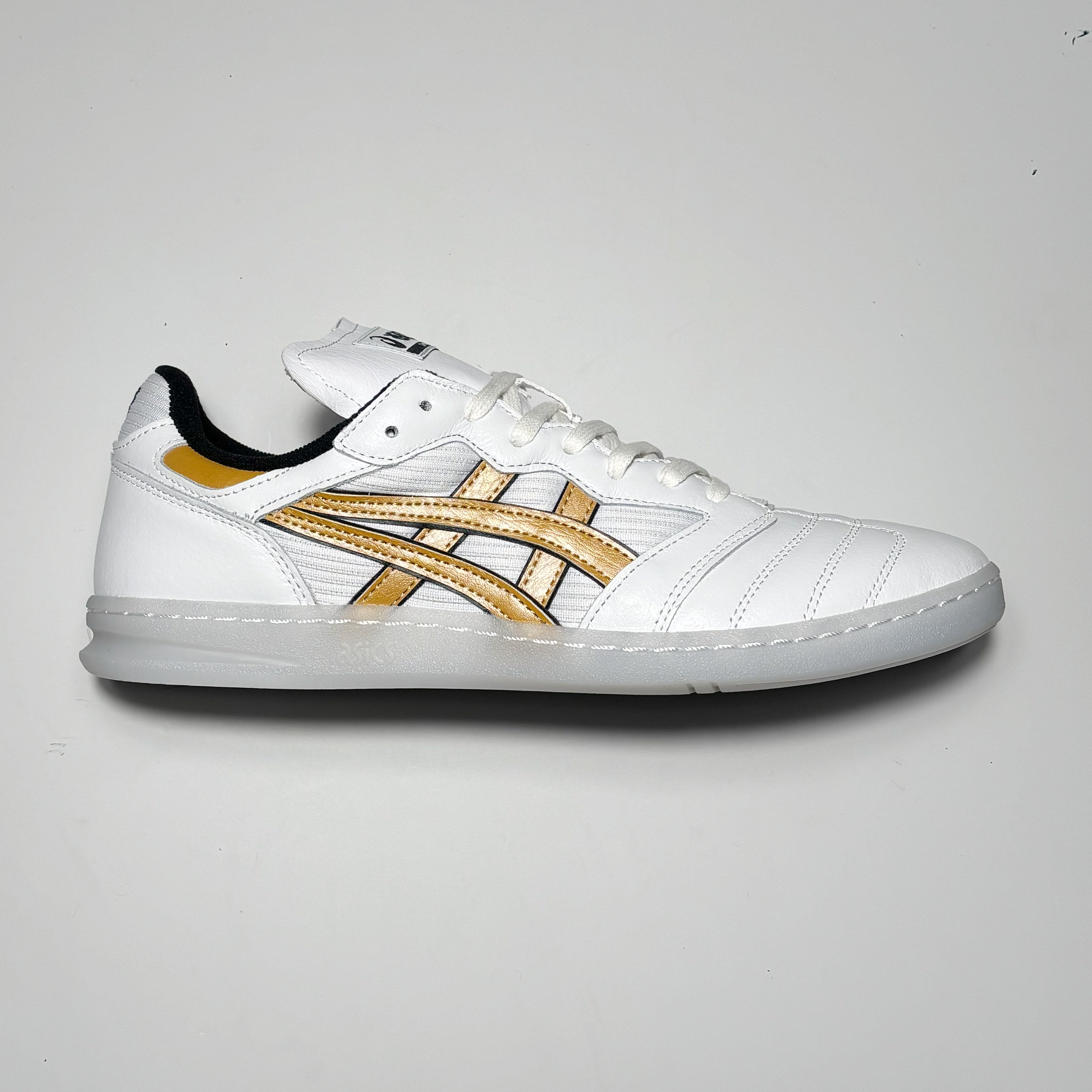 Side image of right shoe. White leather with gold asics branding.