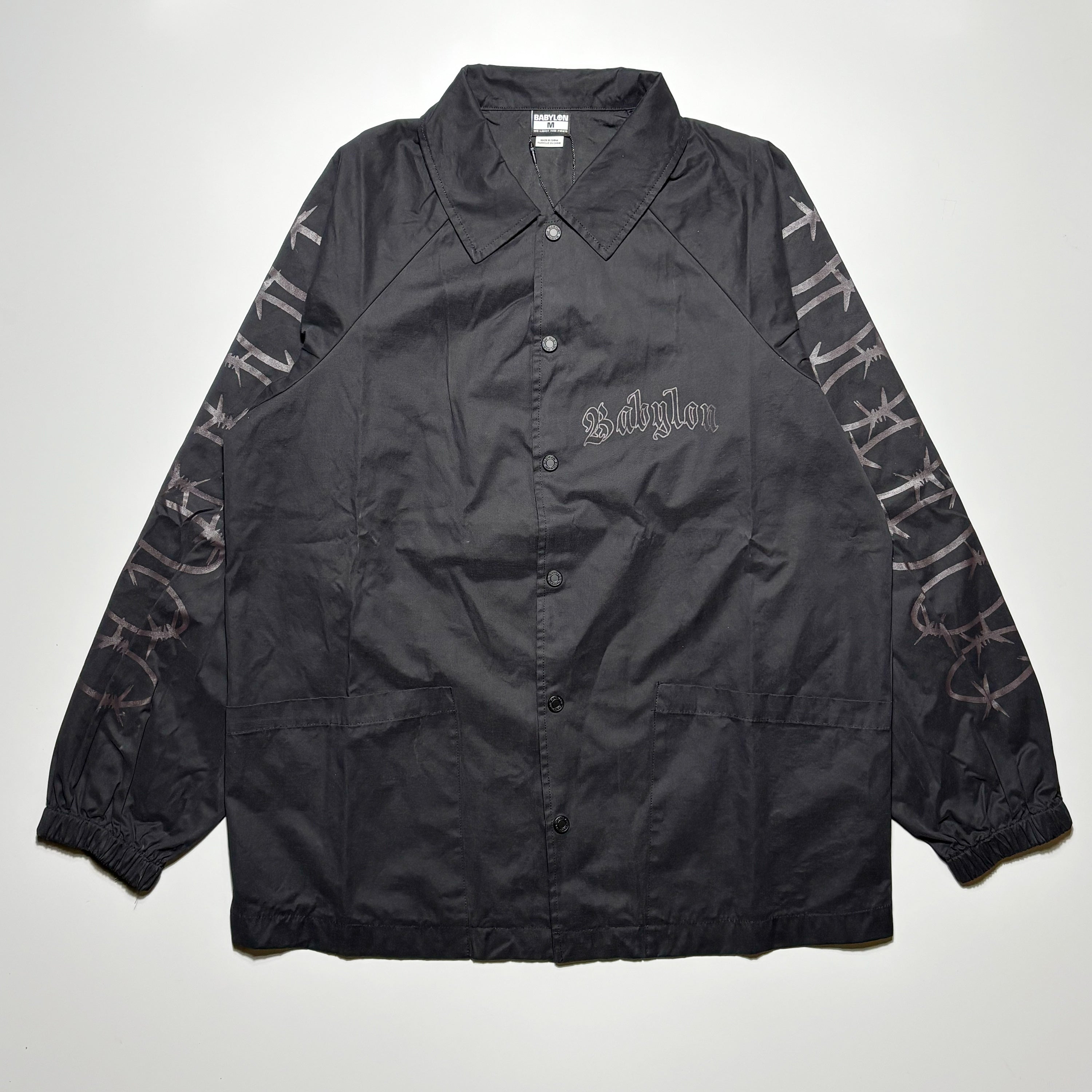 Front image of black coaches jacket with art on chest and sleeves. Button closure.