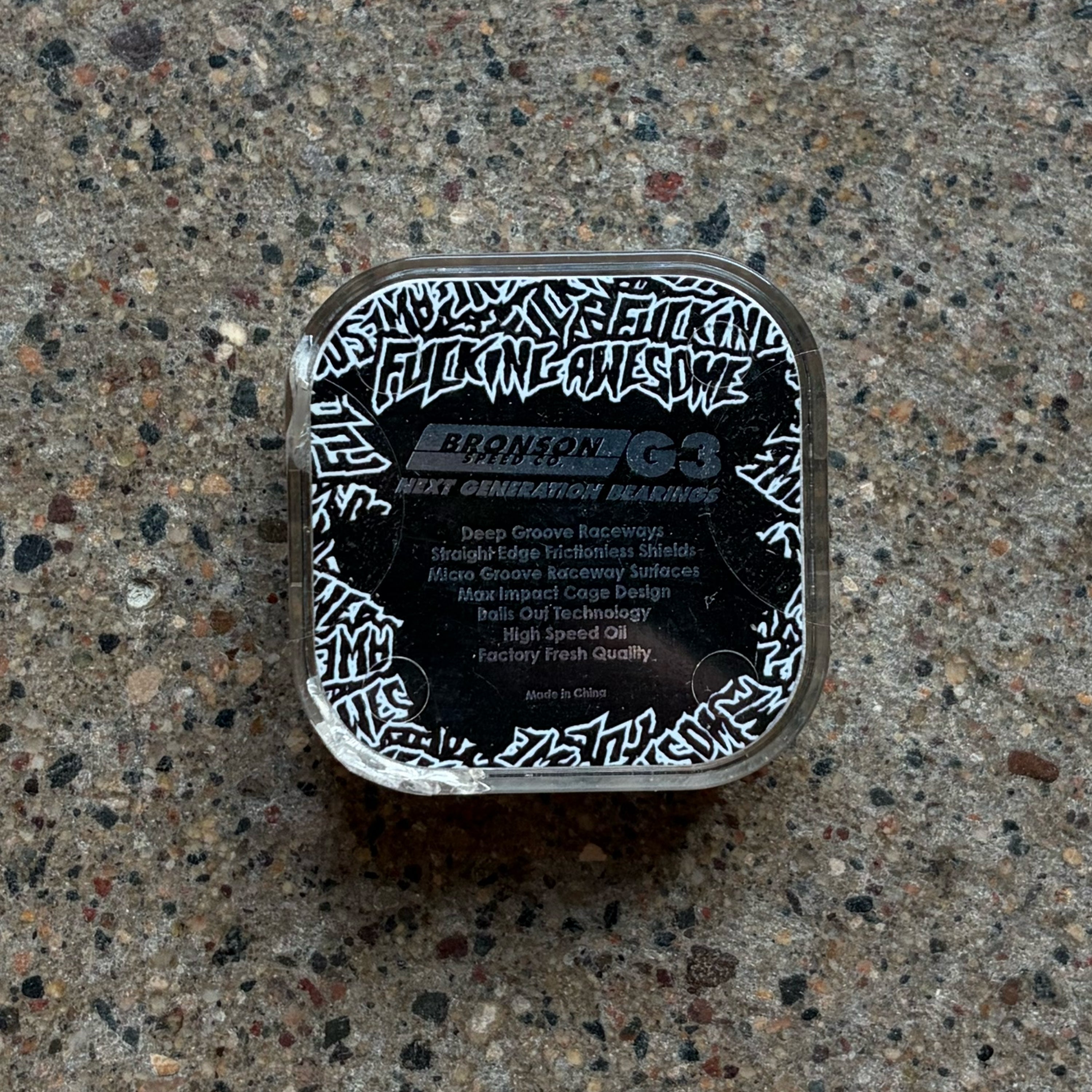 A square plastic tub of Bronson G3 Next Generation Beard Hair Gel with a black and white graphic label, placed on a speckled concrete surface.