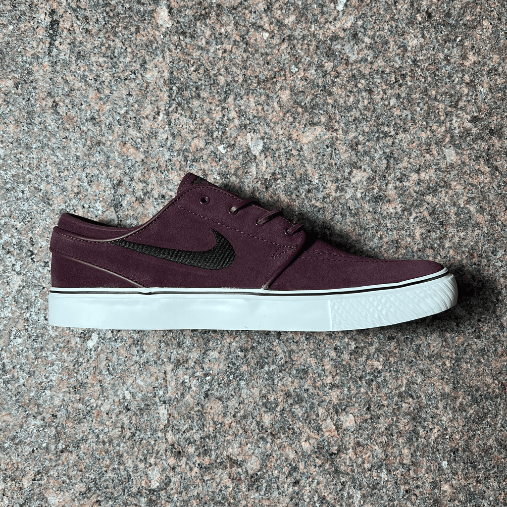 SIDE VIEW OF THE NIKE SB STEFAN JANOSKI PRO MODEL IN BURGUNDY WITH BLACK NIKE SWOOSH AND WHITE SOLE DISPLAYED ON GRANITE