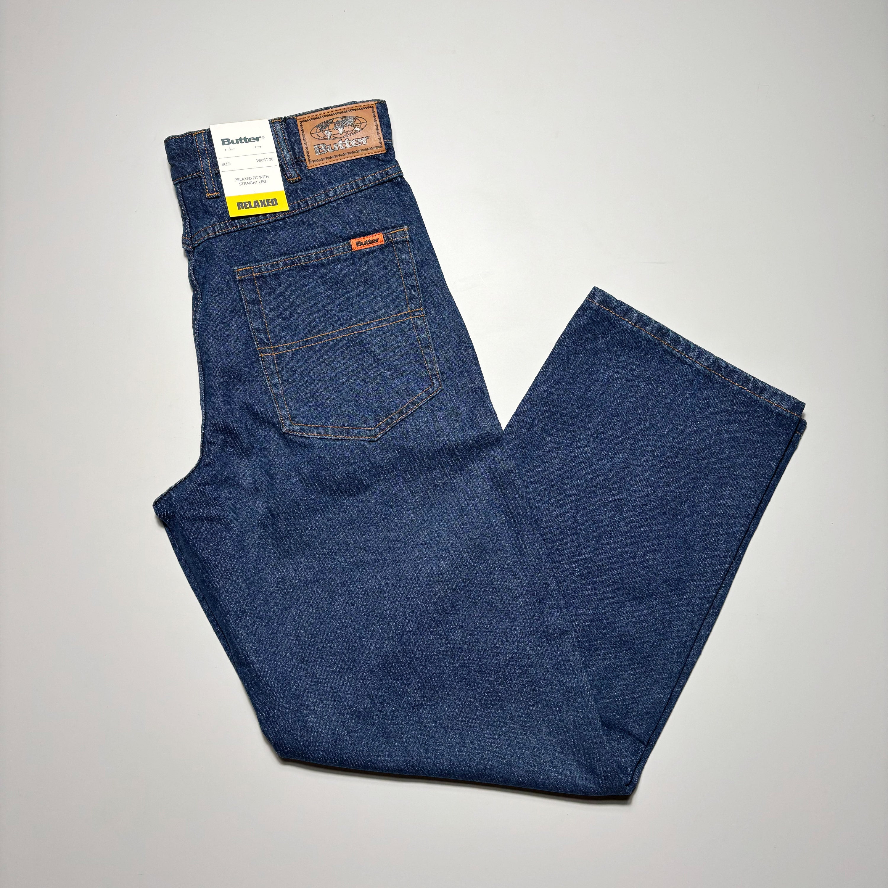 Image of folded dark indigo denim with woven label on back pocket.