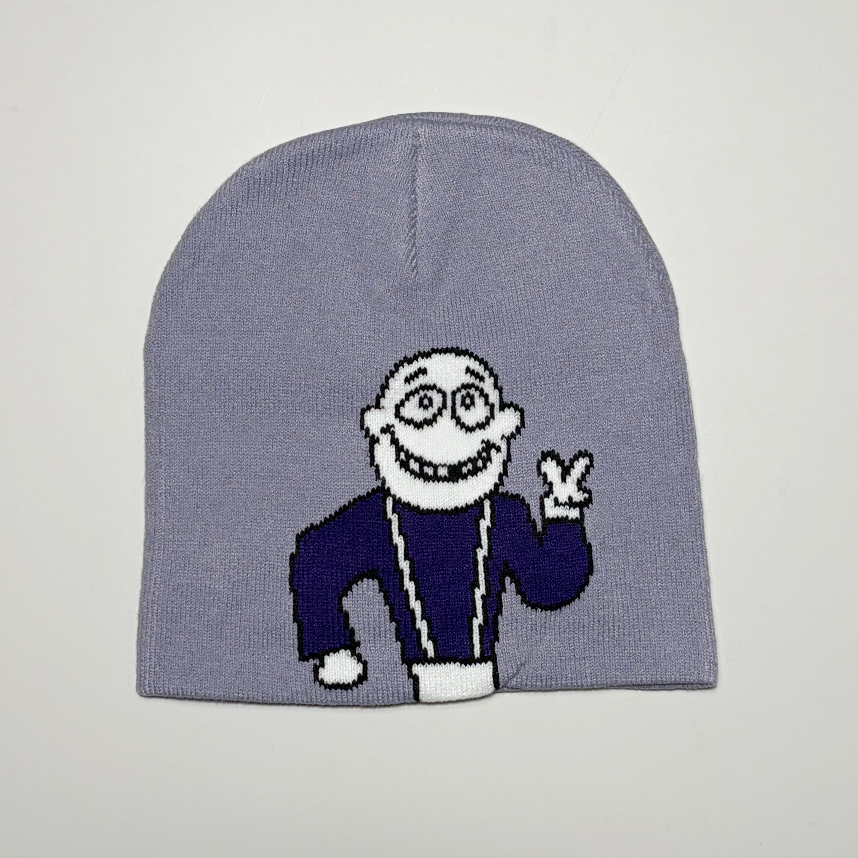 Carpet Company Dinosaur Jr knit beanie featuring a cartoon character knitted onto the front, wearing a dark blue robe and making a peace sign, set against a plain light gray background.
