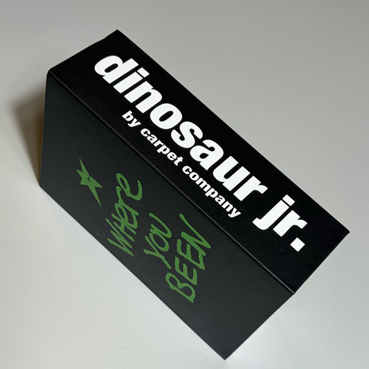 A black rectangular product box with white text reading 'dinosaur jr.' and smaller text 'by carpet company,' plus green handwritten-style text reading 'where you been' on the side, photographed on a light gray background.