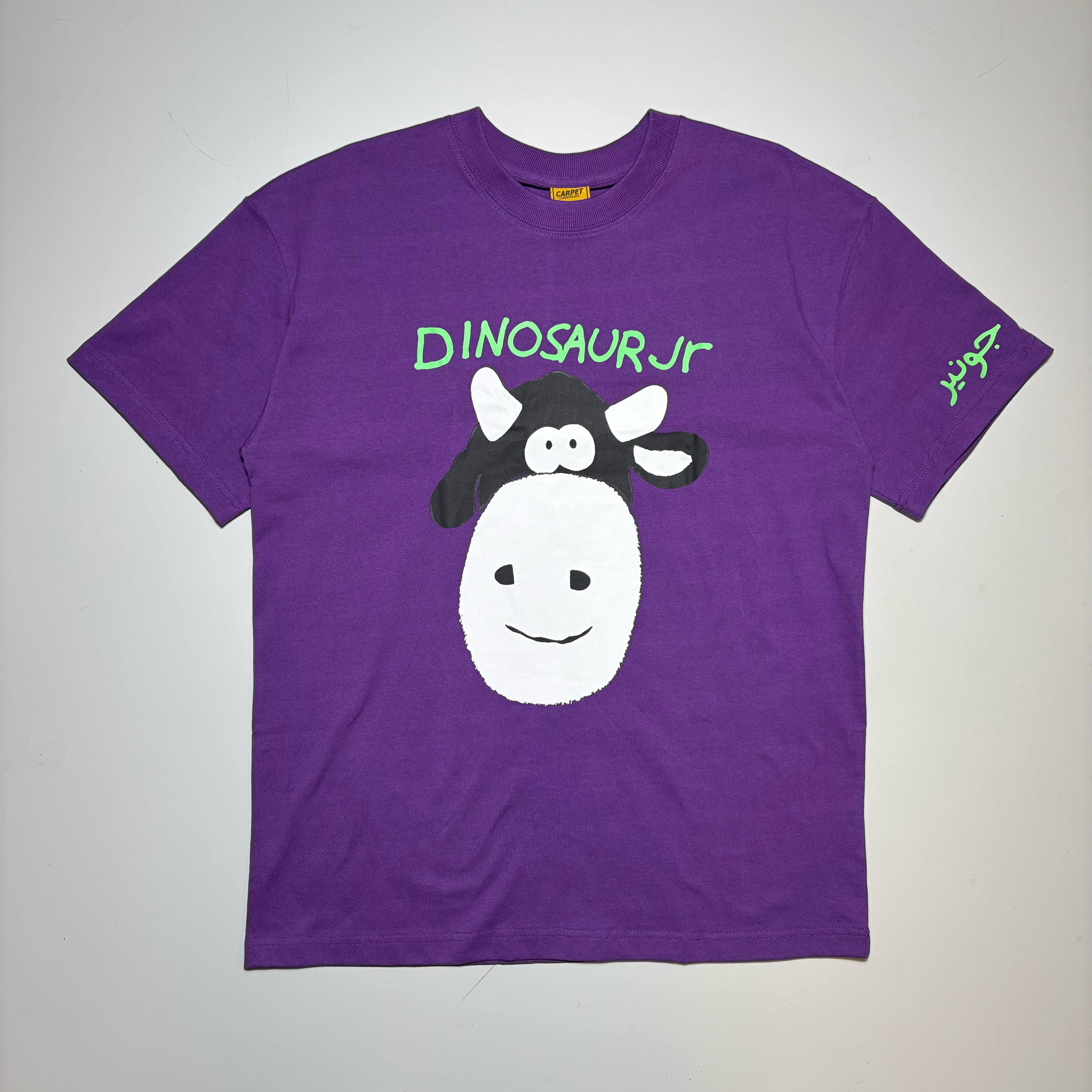A purple short-sleeve t-shirt featuring a cartoon graphic of a cow with a dinosaur head and the text 'DINOSAURJR' in green on the chest, displayed flat against a light gray background.