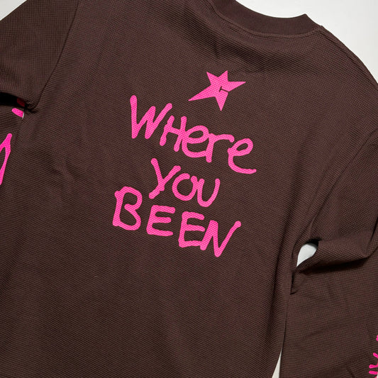 A close-up of a dark brown ribbed long-sleeve shirt showing the back, decorated with a bright pink star and the text 'Where You Been' in matching pink lettering.