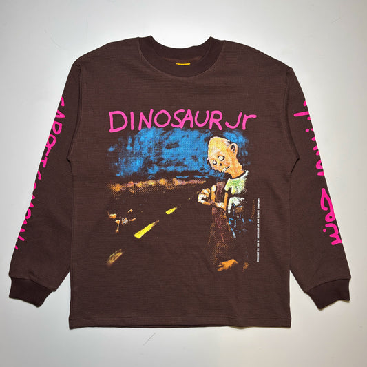 A dark brown long-sleeve graphic t-shirt featuring a cartoon dinosaur character and the text 'DINOSAUR JR' in pink on the front, with pink text down both sleeves, laid flat against a light background.