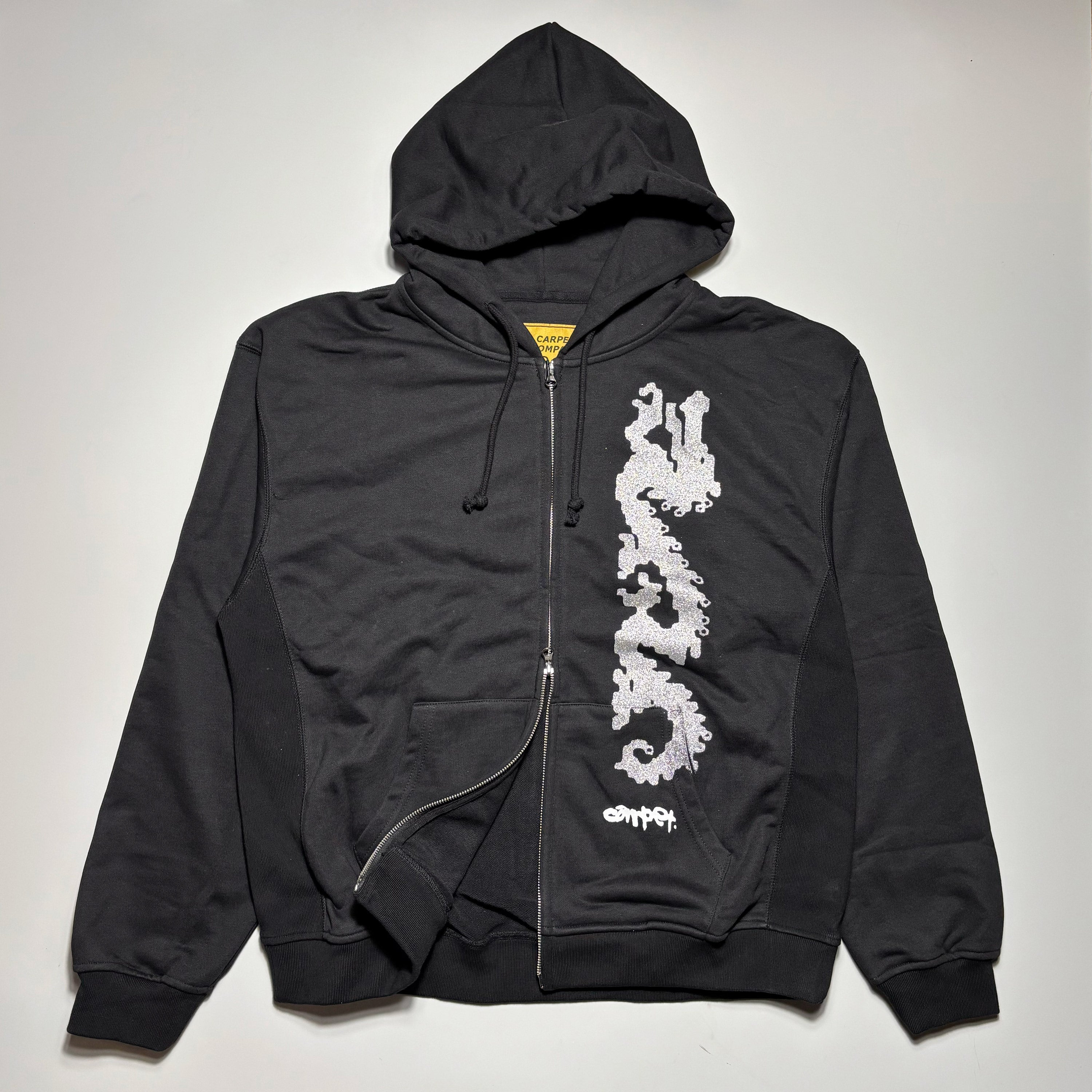 Front image of black zip hoodie with silver art printed on left side.