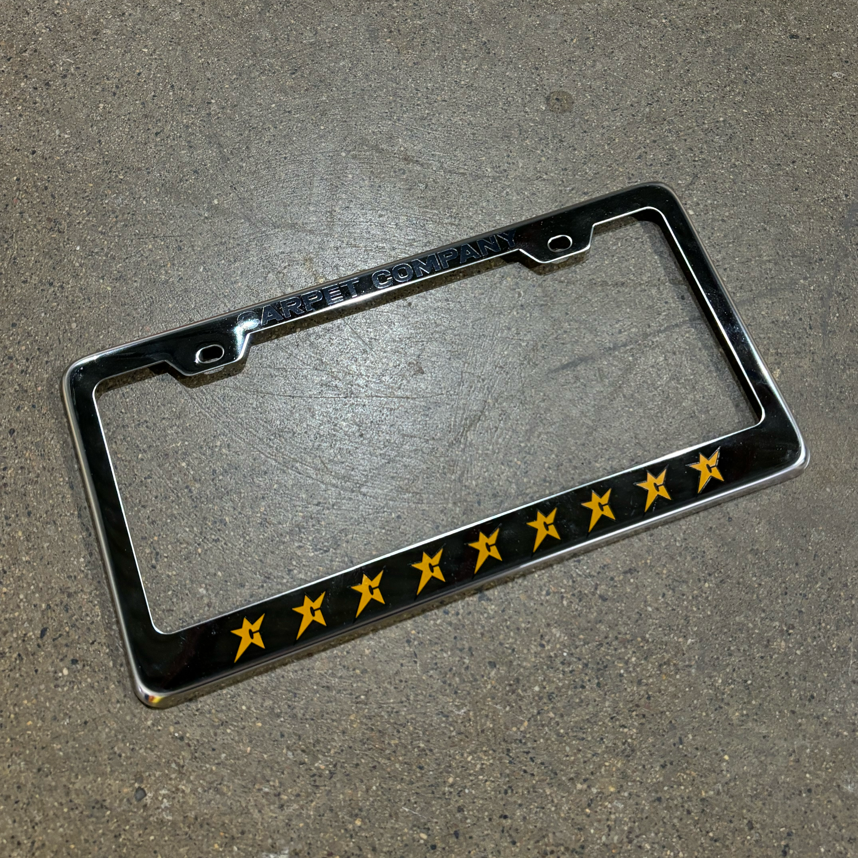 IMAGE OF CHROME PLATED LICENSE FRAME. EMBOSSED CARPET COMPANY FONT AT TOP AND C-STAR LOGOS PRINTED ALONG BOTTOM