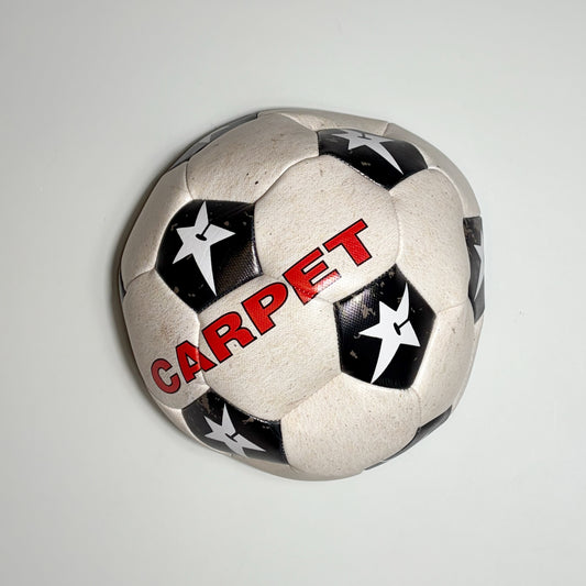 A vintage-style soccer ball with a white base, black star-patterned panels, and the word 'CARPET' printed in red across the front, shown against a plain light gray background.