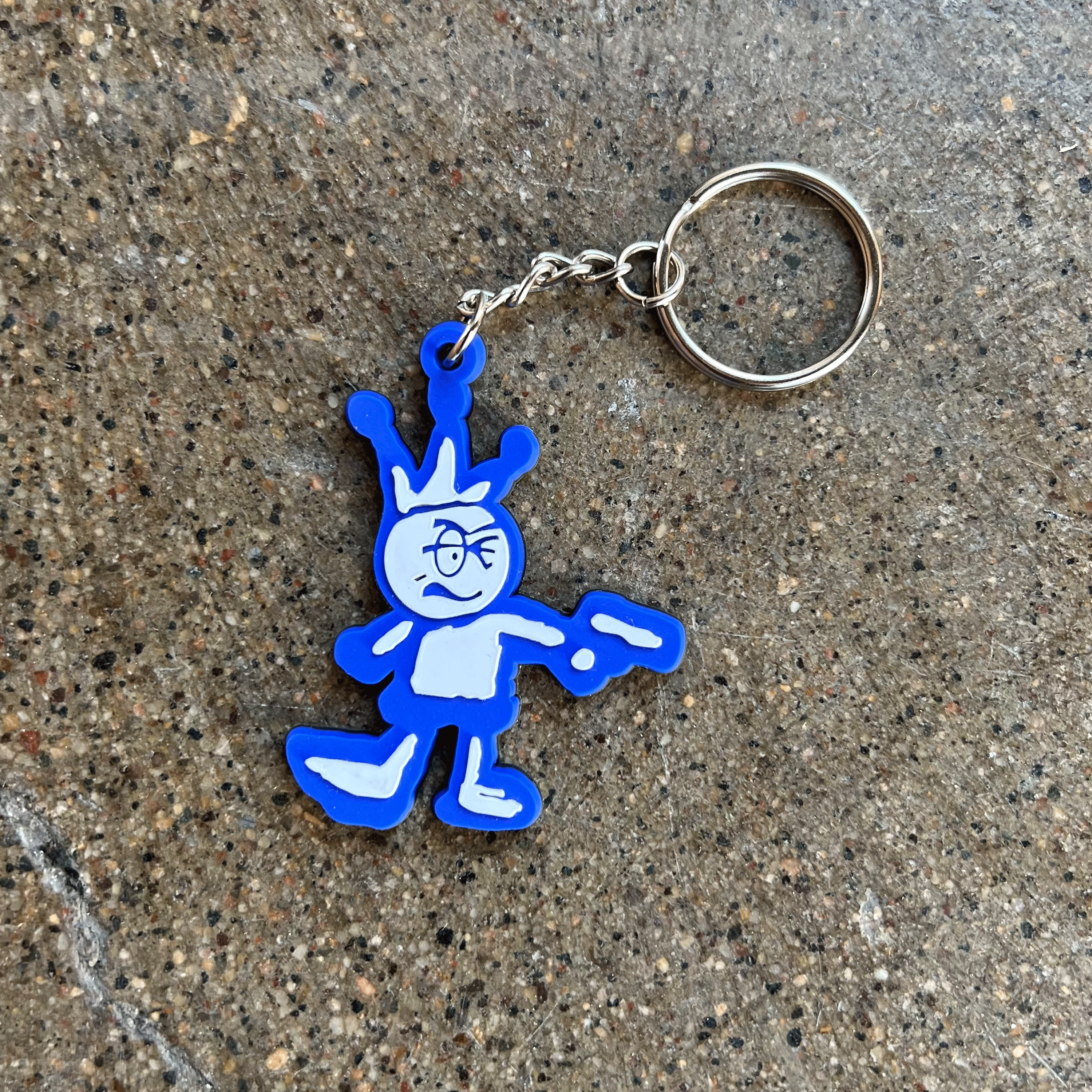 RUBBER CUT CHARACTER OF A CARTOON CHARACTER WITH A CROWN HOLDING A GUN IN BLUE AND WHITE ON METAL KEYCHAIN 