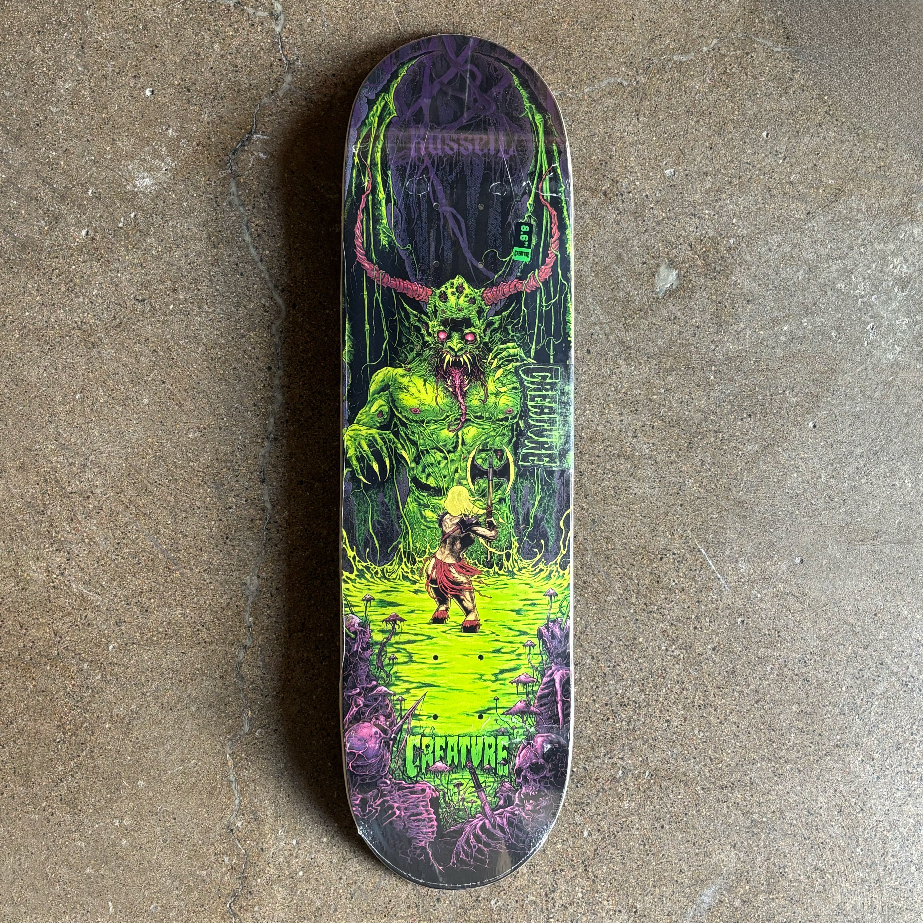 Skateboard deck with a colorful design featuring a creature on a concrete surface