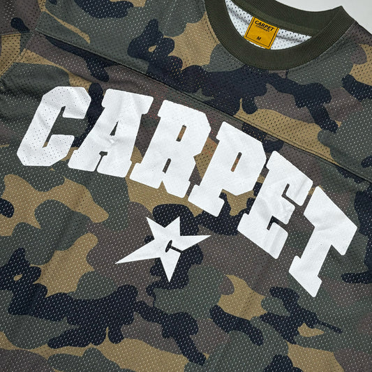 Close-up of a camouflage mesh jersey with large white 'CARPET' lettering and a white star logo on the front. The shirt has a green collar and a yellow neck label.