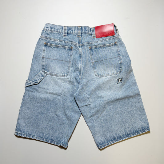 Light blue denim shorts shown from the back, featuring a red leather brand patch at the waistband, a small embroidered logo on the back pocket, and a light beige background.