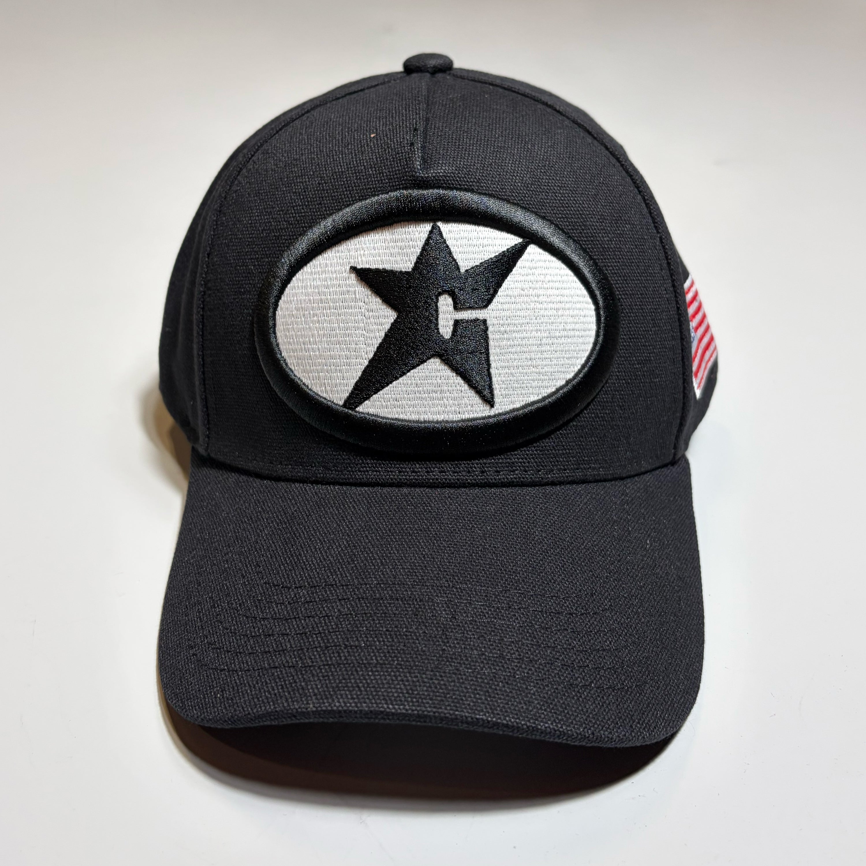 Front image of black snapback hat with c-star patch on crown. Glow in the dark oval logo. Carpet Company Season 22