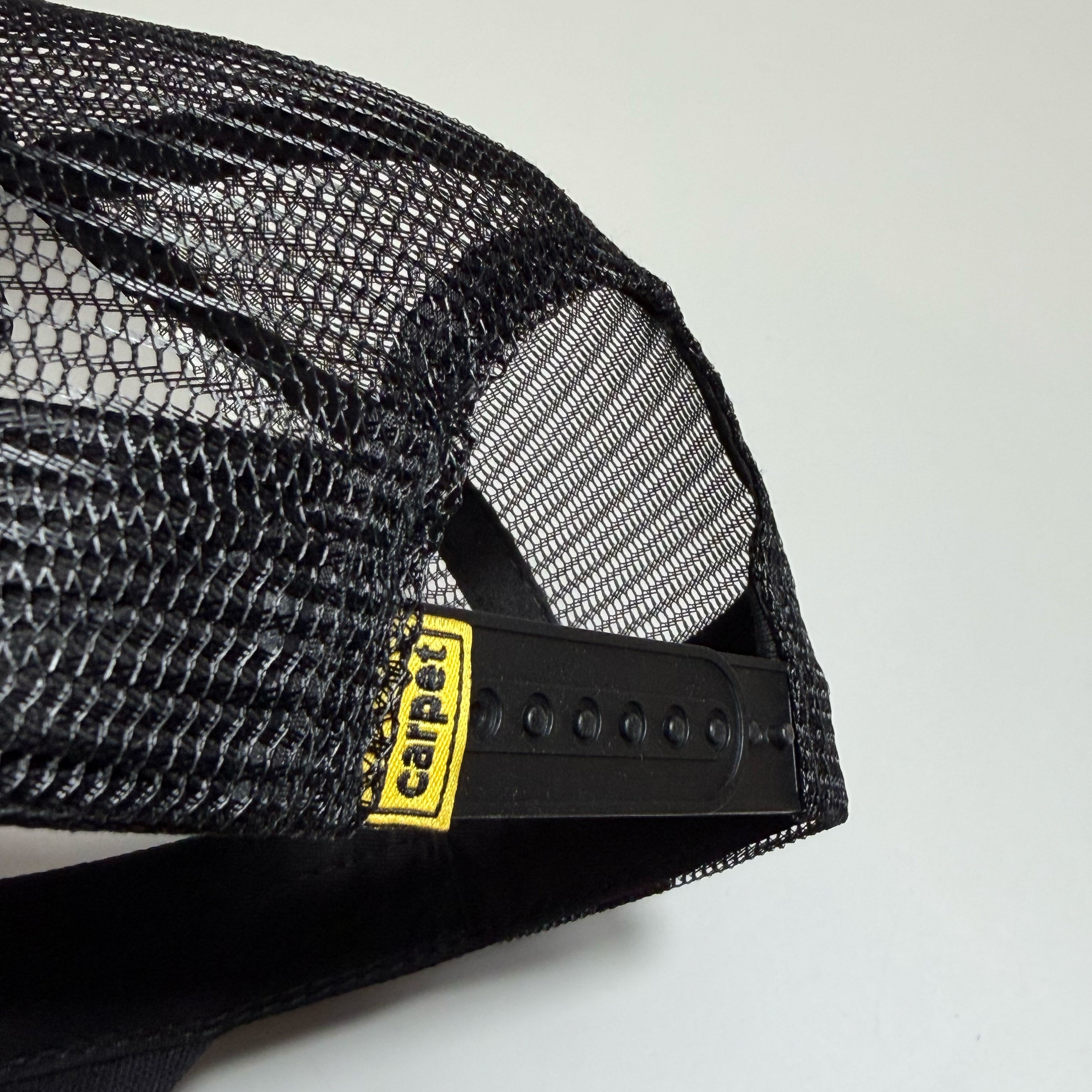 Close-up of a black mesh trucker hat showing the back strap adjustment area with a yellow and black Carhartt logo patch.