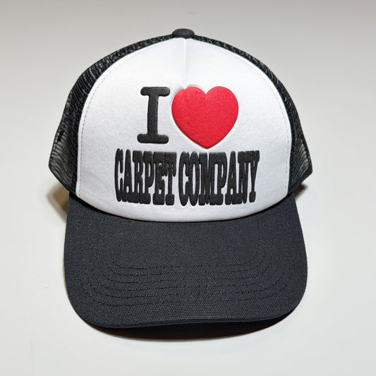 Front image of black/white trucker hat. I heart carpet company in puff printed ink on crown.
