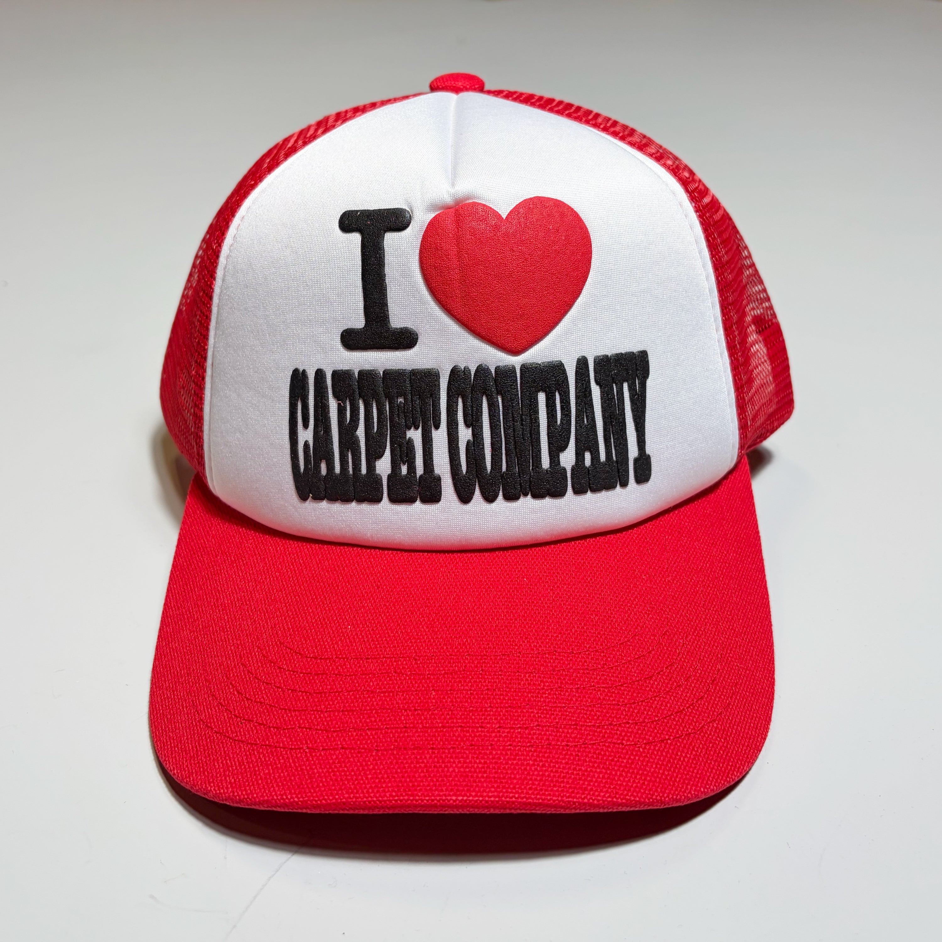 Front image of red/white trucker hat. I heart carpet company in puff printed ink on crown. 
