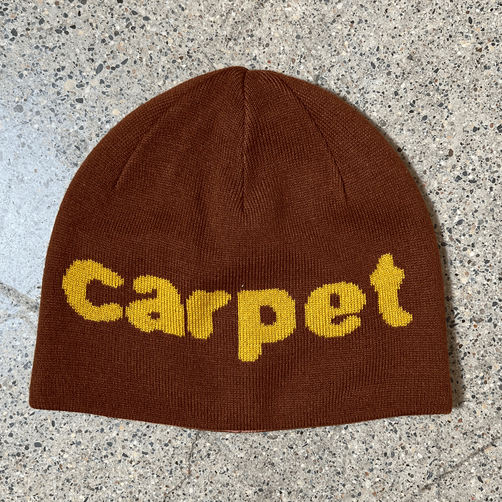 Image of brown side of beanie with carpet font woven in yellow