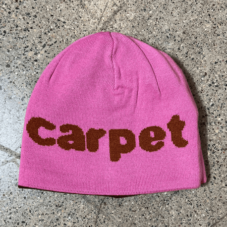 Image of reverse side of beanie, pink with carpet font woven in brown