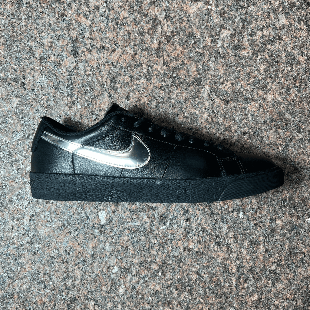 SINGLE NIKE SB BLAZER LOW SHOE IN BLACK LEATHER AND BLACK SOLE WITH REFLECTIVE SWOOSH DISPLAYED ON GRANITE