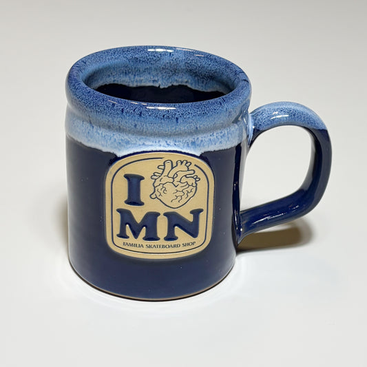 A dark blue glazed ceramic mug with a cream-colored 'I MN' logo patch on the front, featuring a heart graphic and the text 'FAMILIA SKATEBOARD SHOP'.