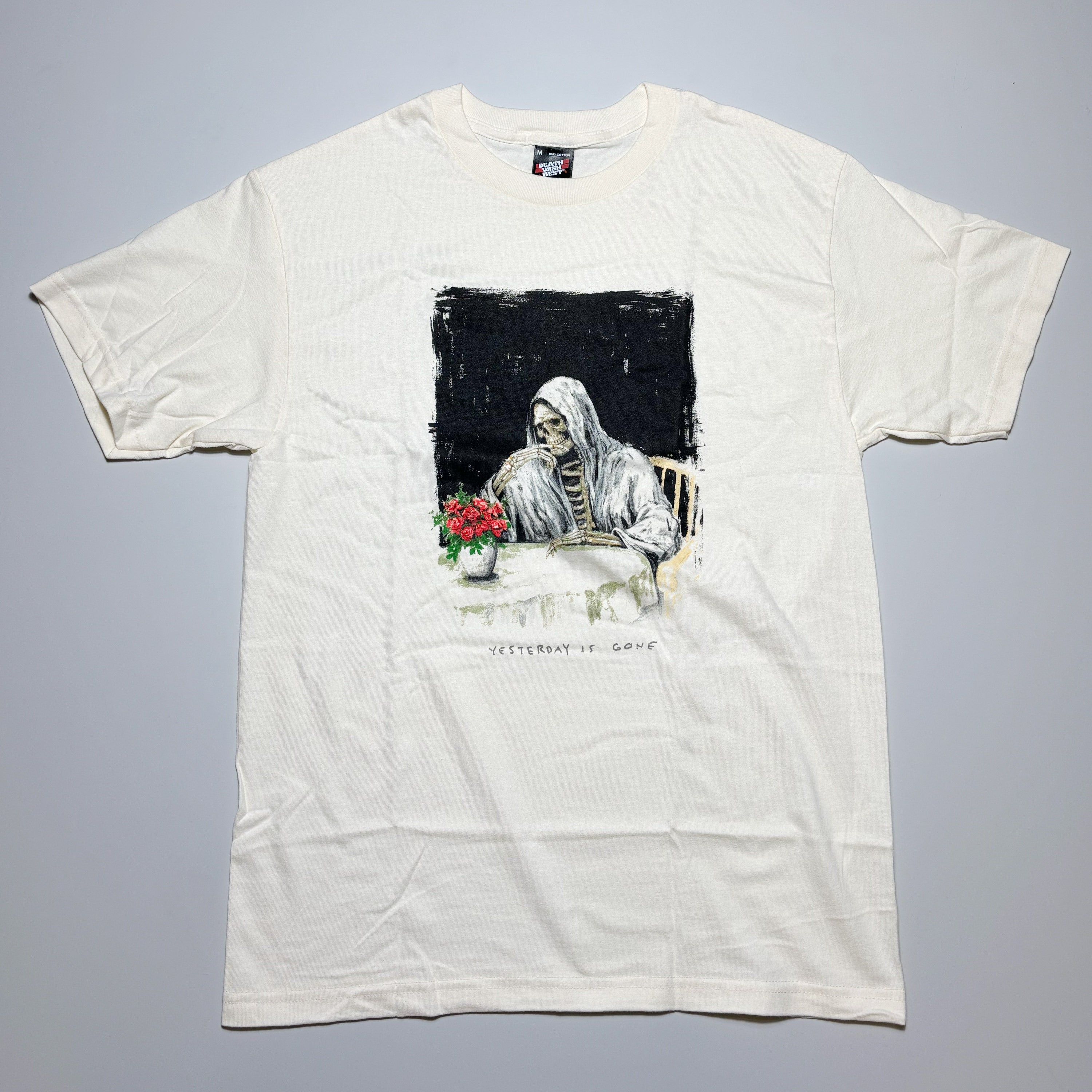 White t-shirt with a graphic of a skeleton holding flowers on a gray background