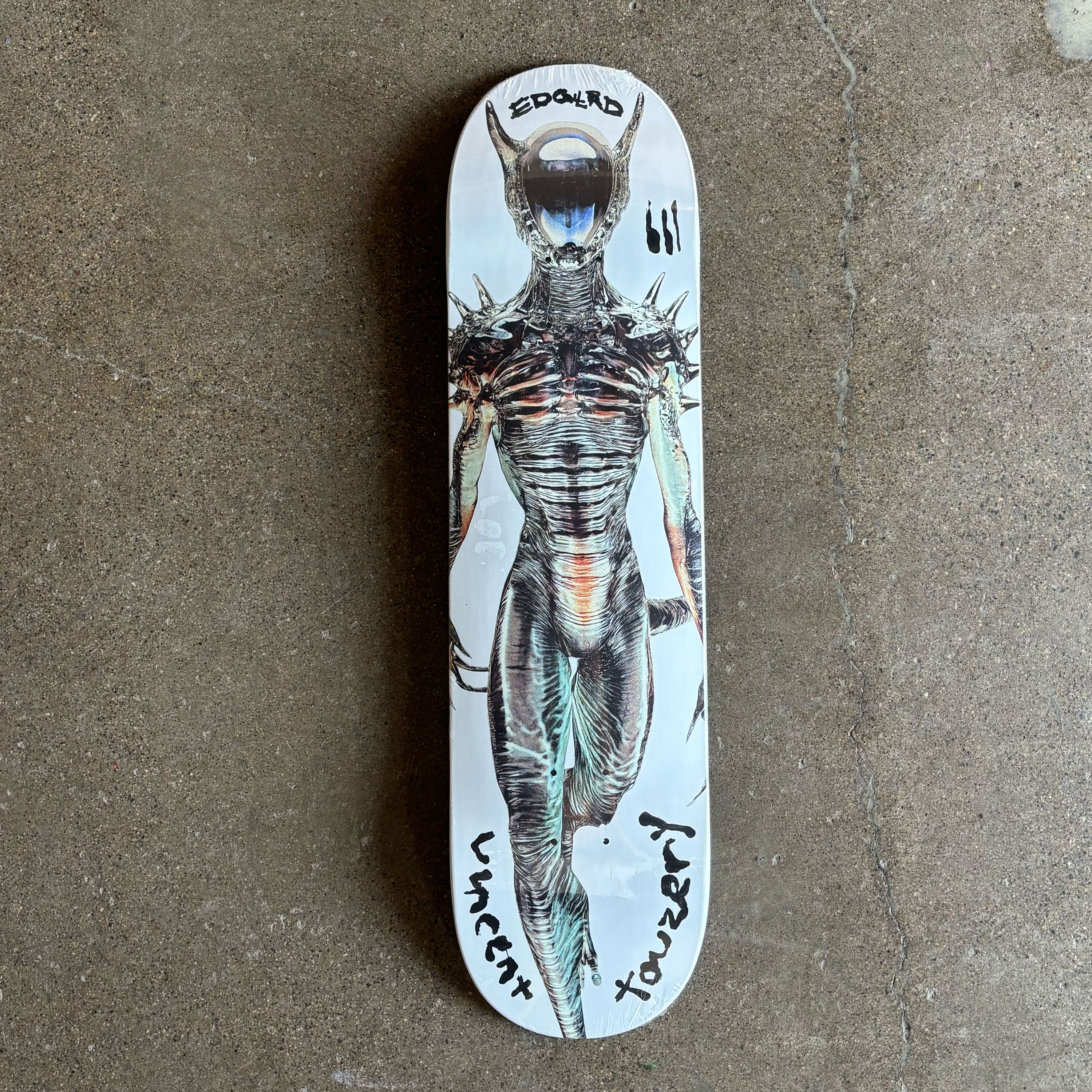 Full image of white deck with alien art from top to bottom. Vincent Touzery text on tail in black.