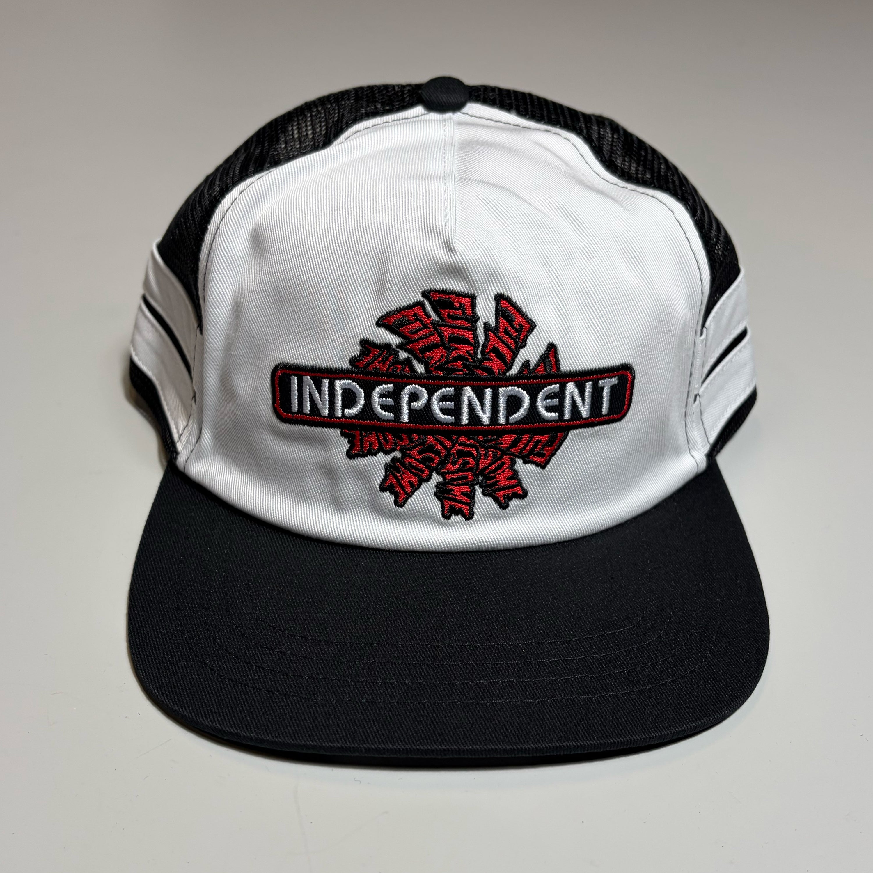 Fucking Awesome brand black and white trucker hat featuring a prominent red and black embroidered 'INDEPENDENT' logo patch on the front panel, set against a neutral light gray background.