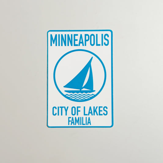 Sign with 'Minneapolis City of Lakes Familia' text and a sailboat icon on a gray background