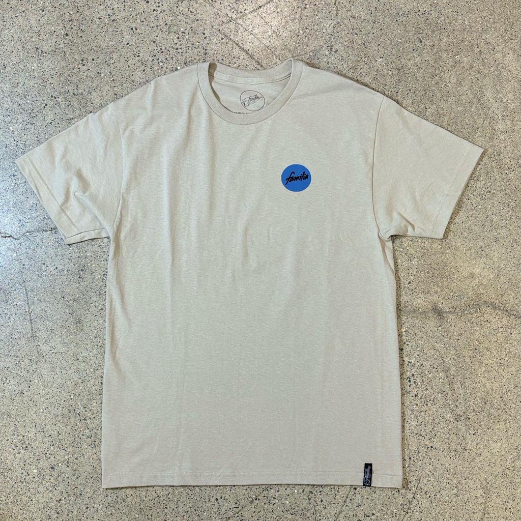 FRONT SIDE OF SAND COLOR T-SHIRT WITH A SMALL BLUE CIRCLE GRAPHIC THAT READS FAMILIA