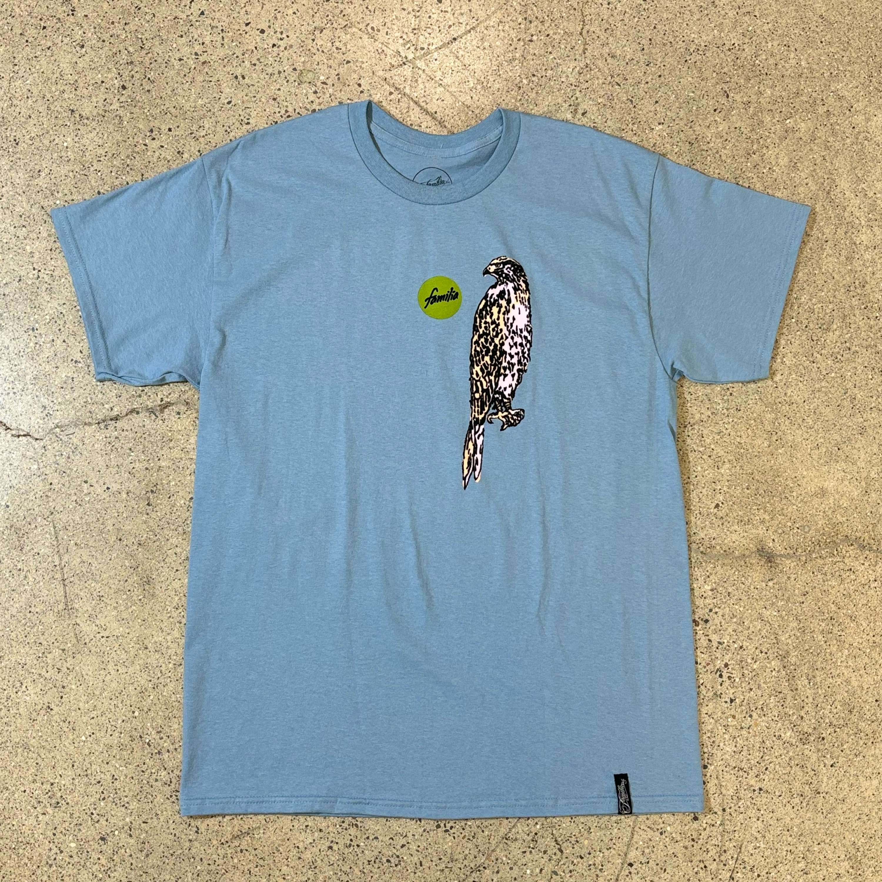 FRONT SIDE OF A BLUE T-SHIRT WITH A CENTER CHEST GRAPHIC OF A CIRCLE THAT READS FAMILIA AND A PAINTED STYLED HAWK 