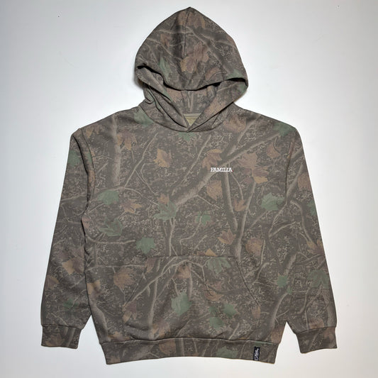 A camouflage hoodie with a woodland branch and leaf pattern in shades of brown, green, and gray, featuring a small white 'FAMILIA' logo on the left chest, laid flat against a light gray background.