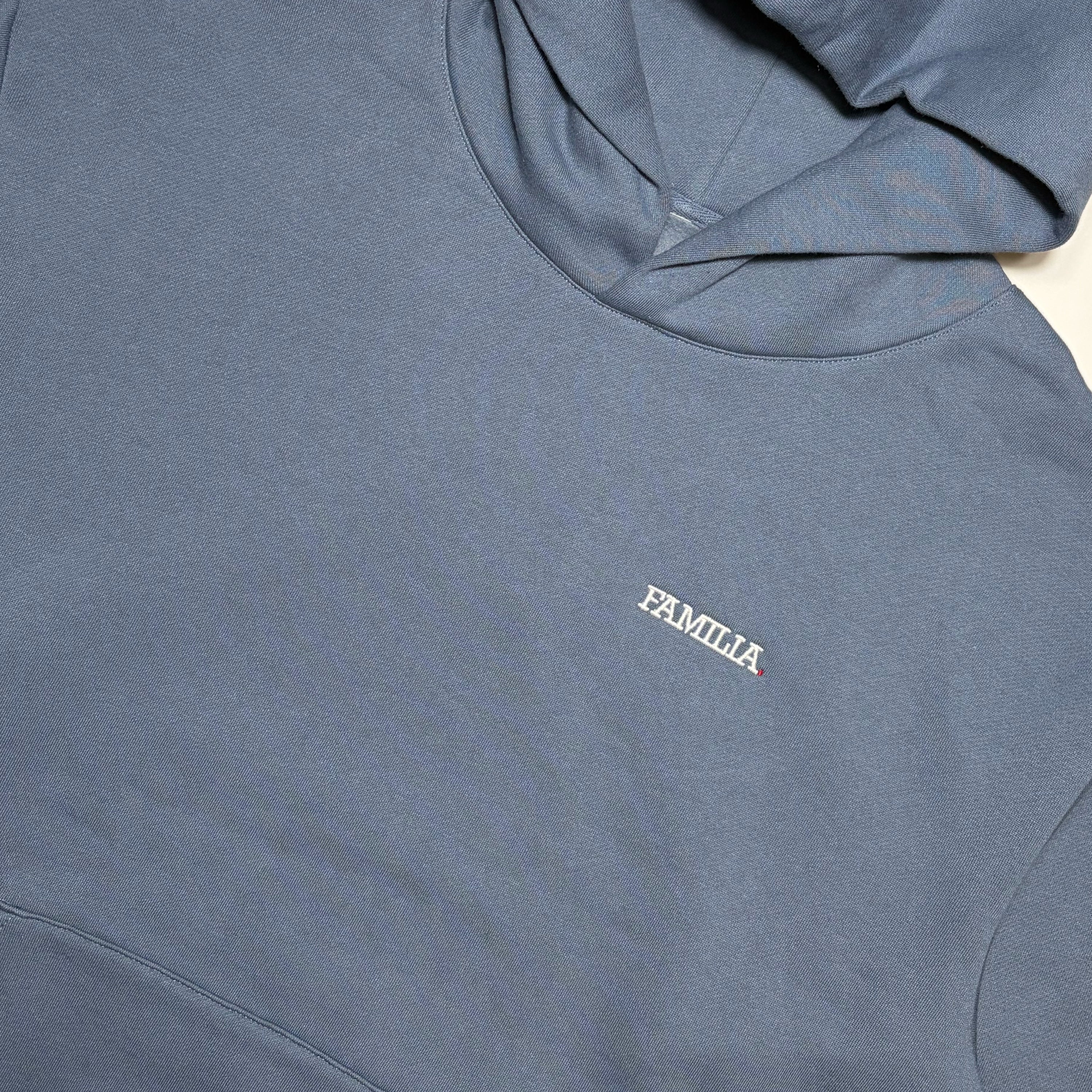 Close up detail of blue hoodie with 'FAMILIA' embroidered in white on chest.