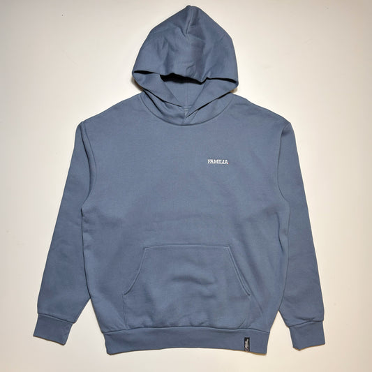 A dusty blue pullover hoodie with a small white 'FAMILIA' text logo on the left chest, laid flat against a light beige background.