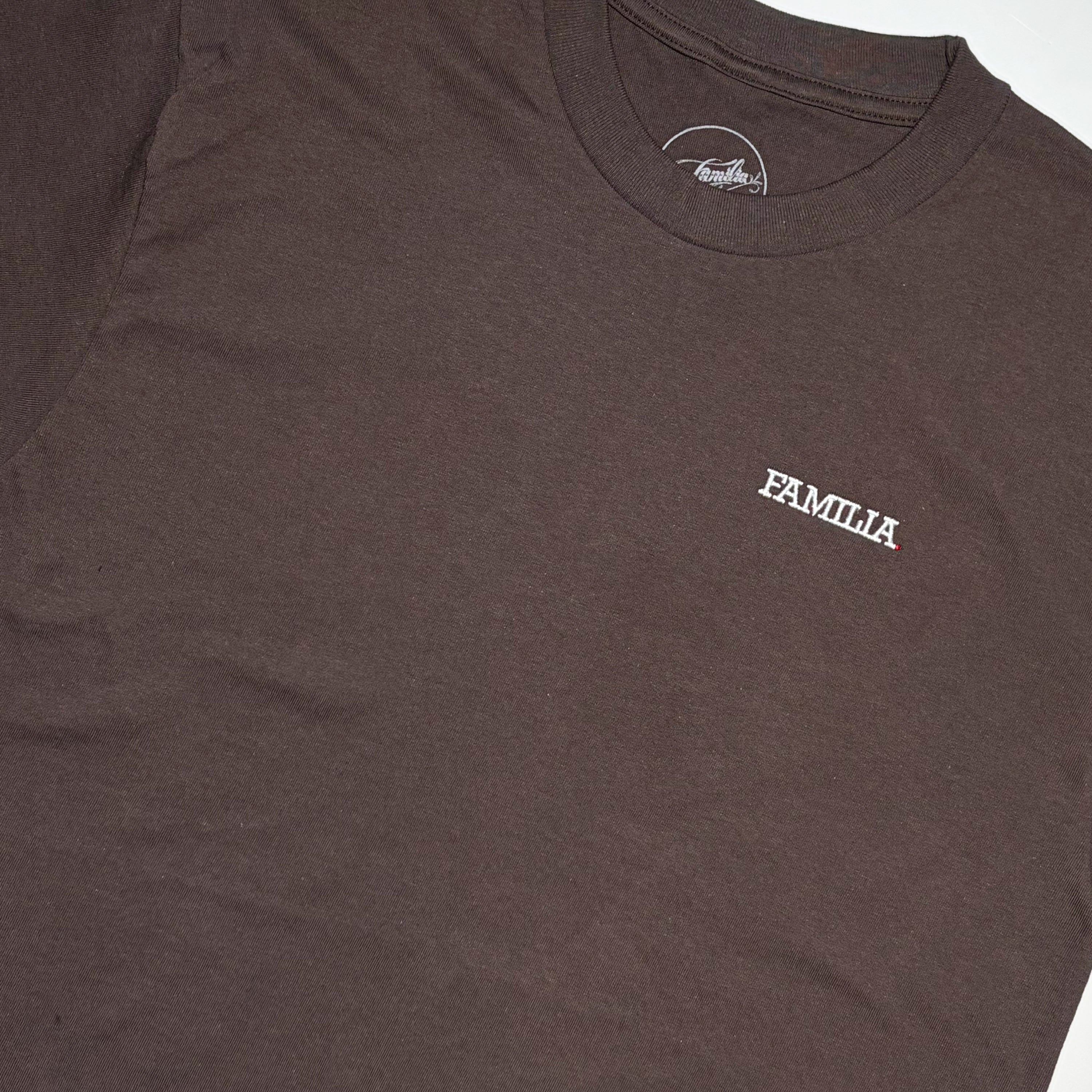 Close up detail of dark brown t-shirt with 'FAMILIA' embroidered logo in white on chest.