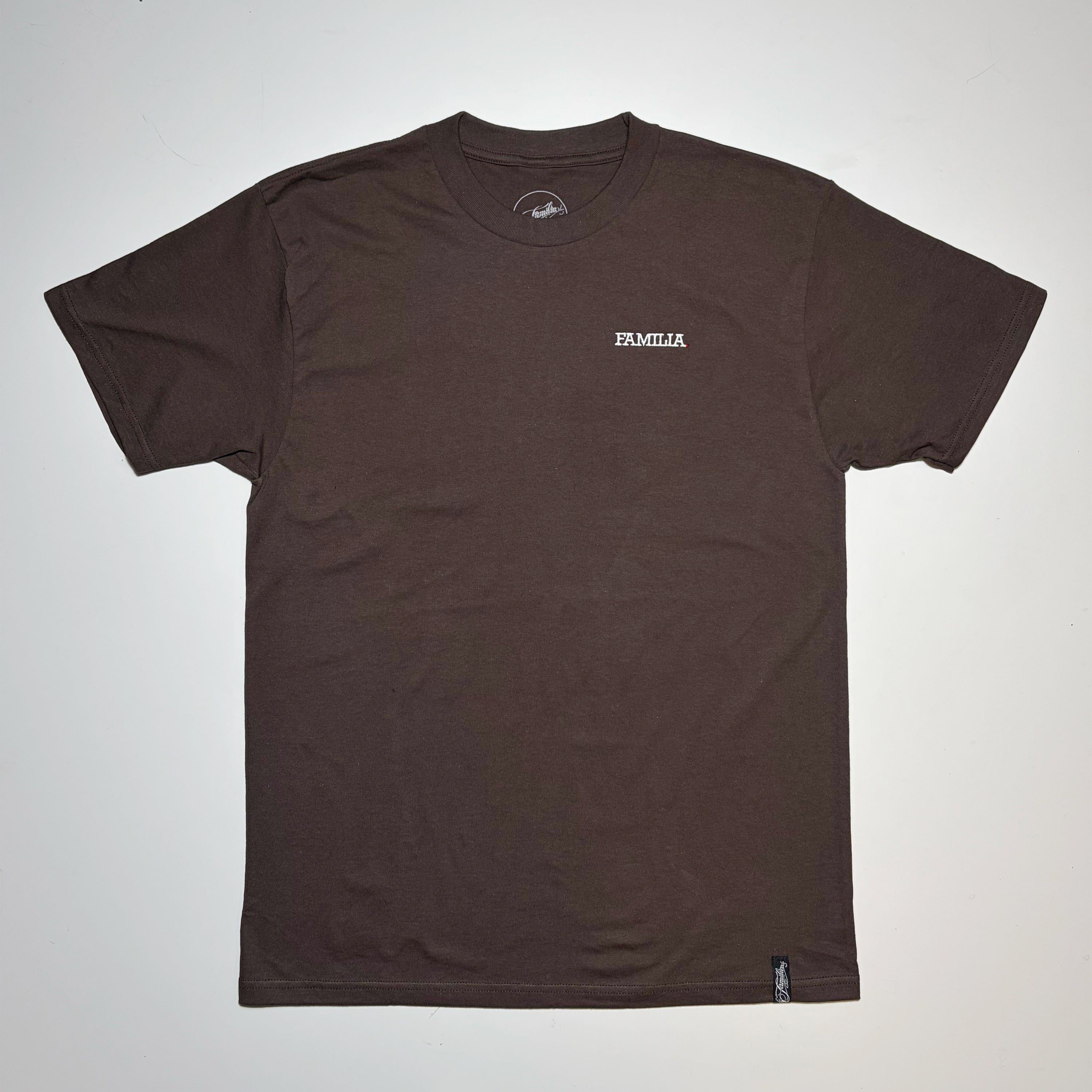 A dark brown short-sleeve t-shirt with a small white 'FAMILIA' logo embroidered on the left chest, laid flat against a light gray background.