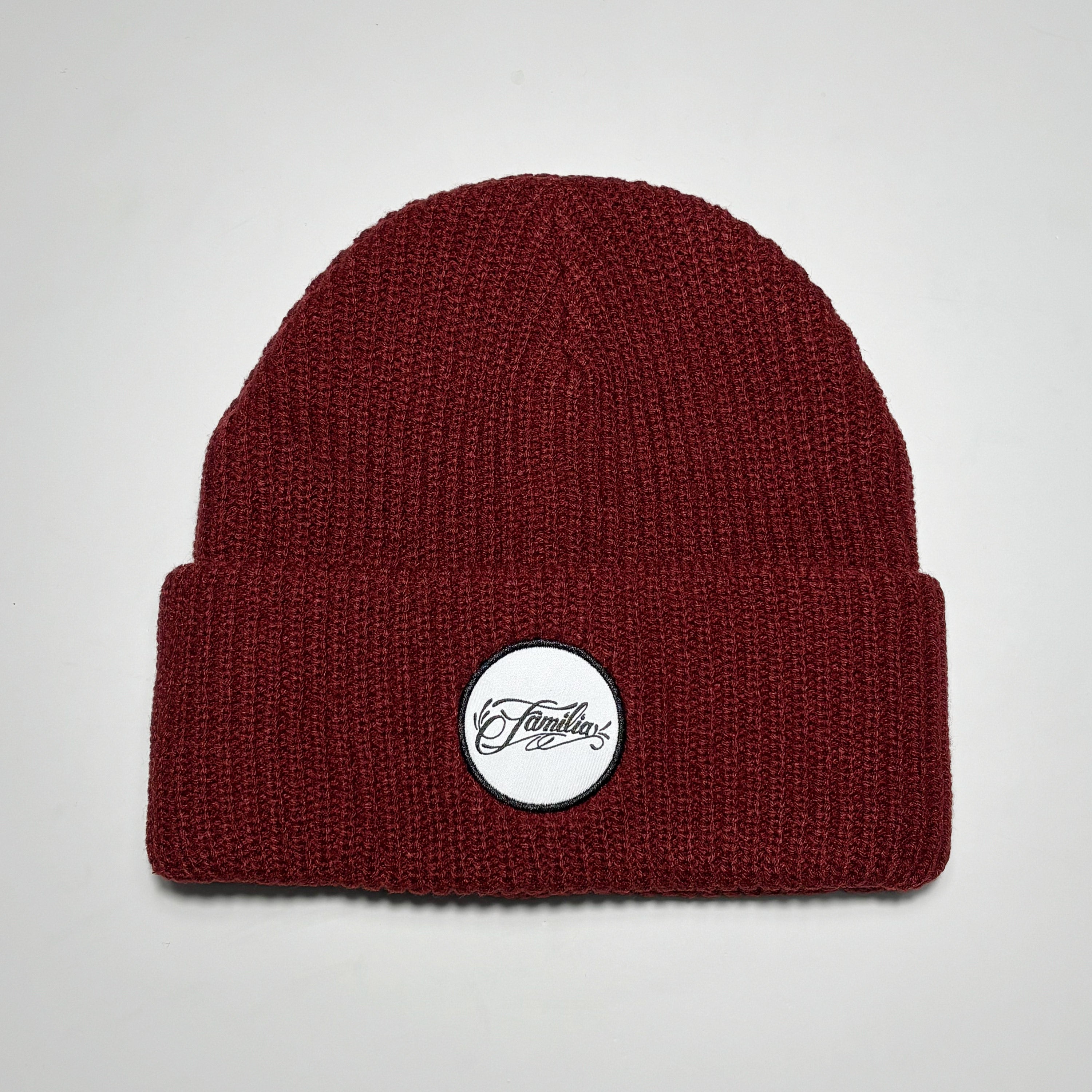 Maroon colored beanie with white and black familia script patch.