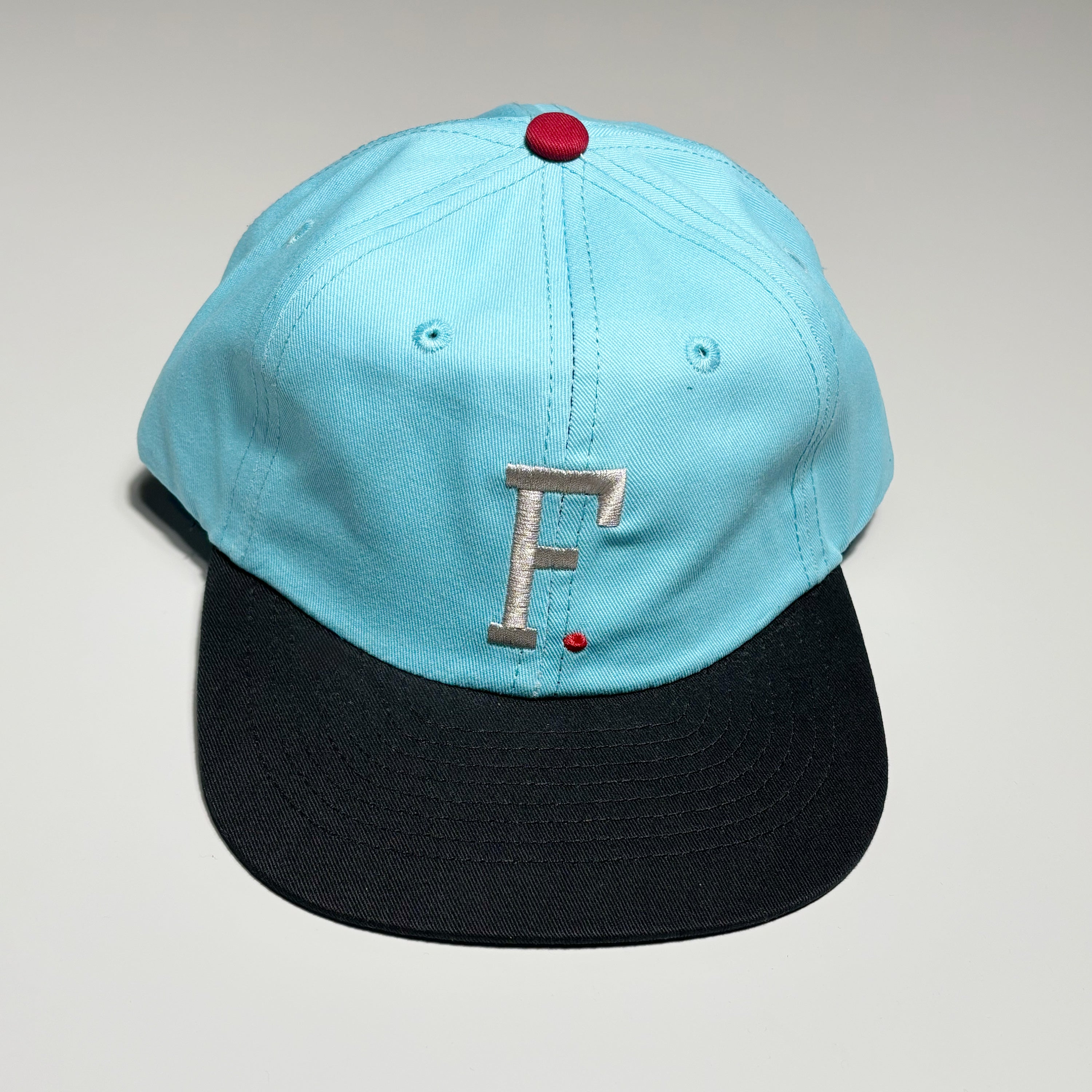 Front image of blue hat with embroidered logo on crown and black brim.
