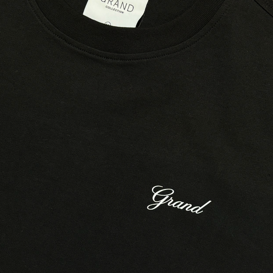 CLOSE UP ANGLE OF BLACK T-SHIRT, GRAPHIC IN CURSIVE FONT THAT READS GRAND ON LEFT CHEST