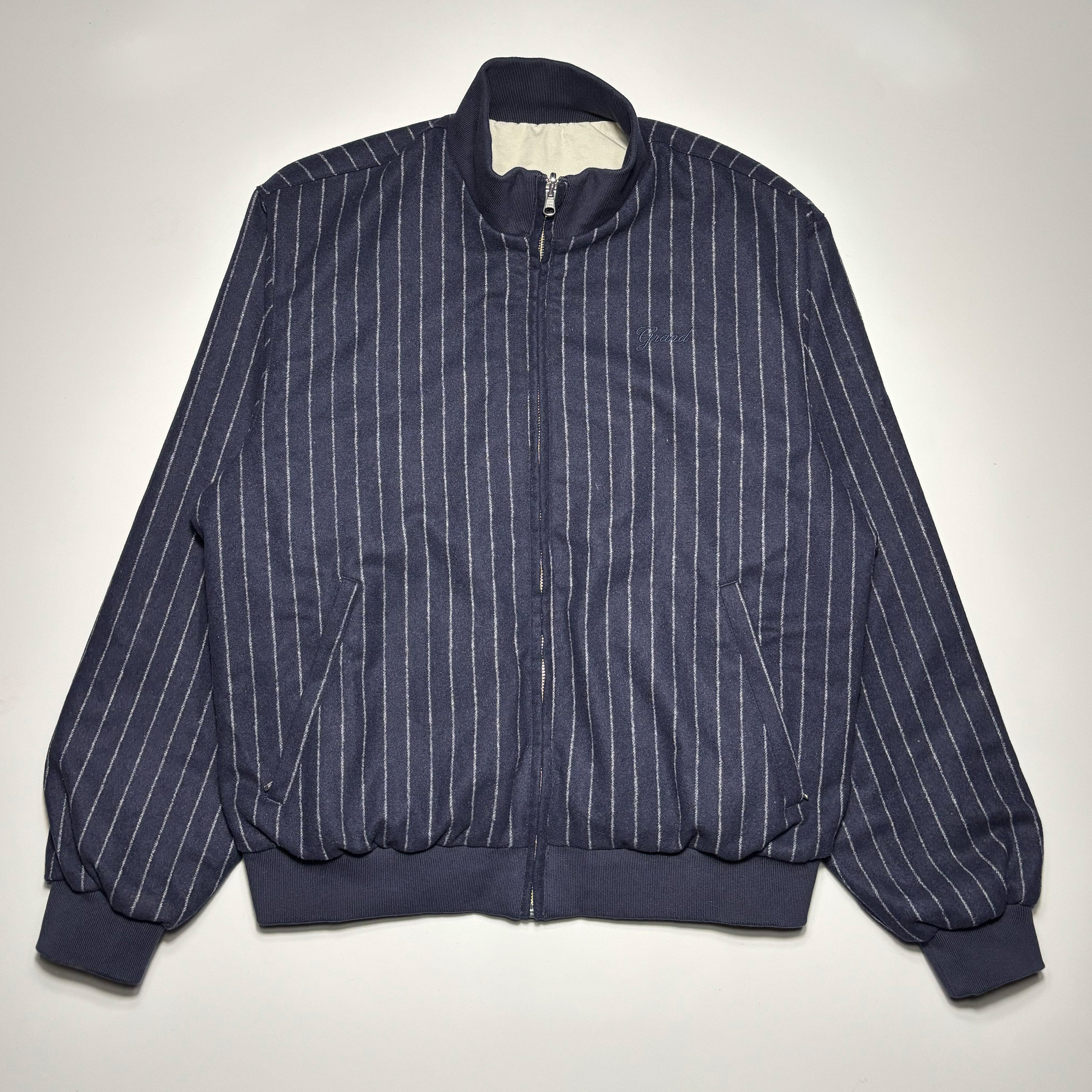 Front image of navy wool jacket with white pinstripes and embroidered logo on chest.