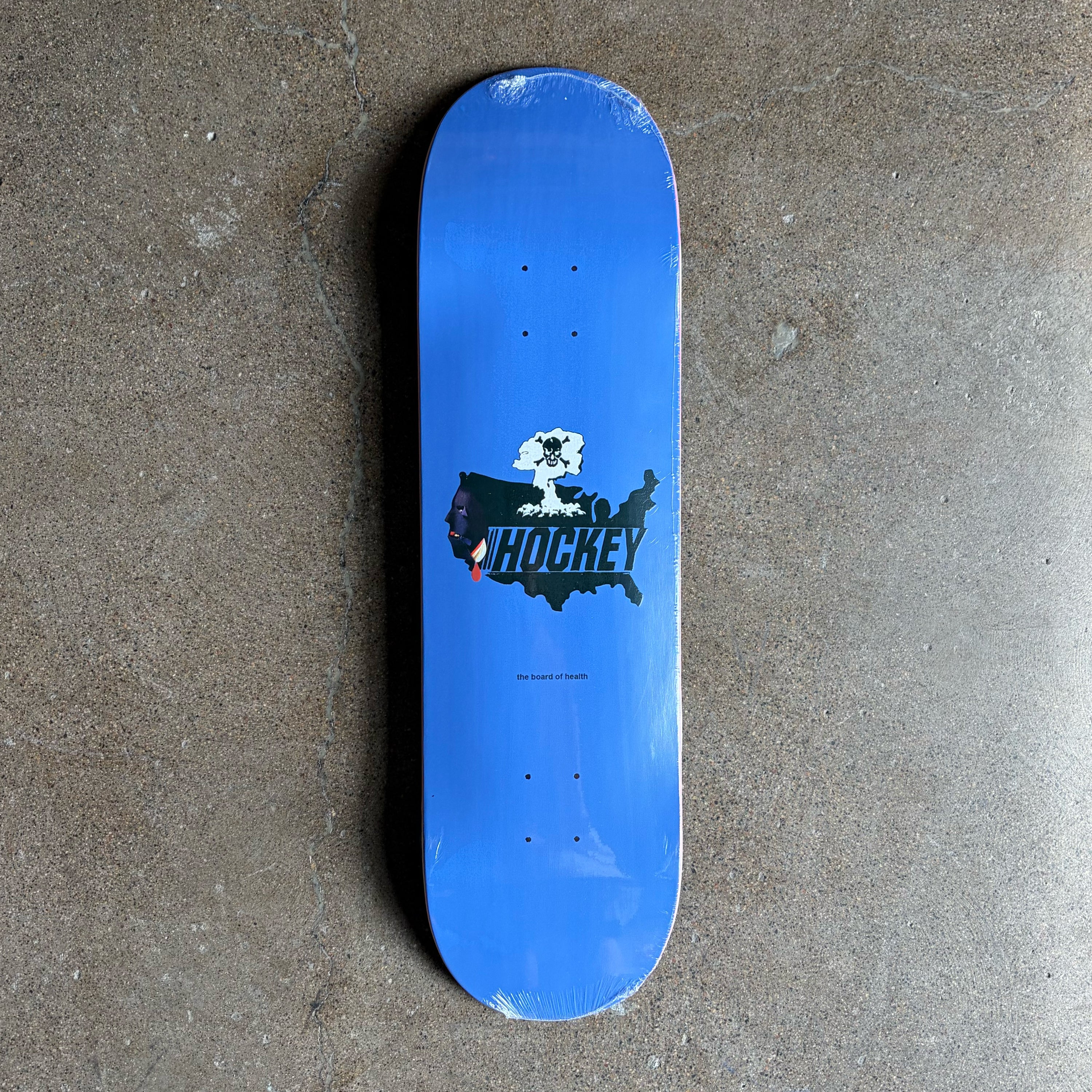 A blue skateboard deck with a black, white, and red 'HOCKEY' graphic on the underside, photographed from directly above on a textured gray concrete floor.