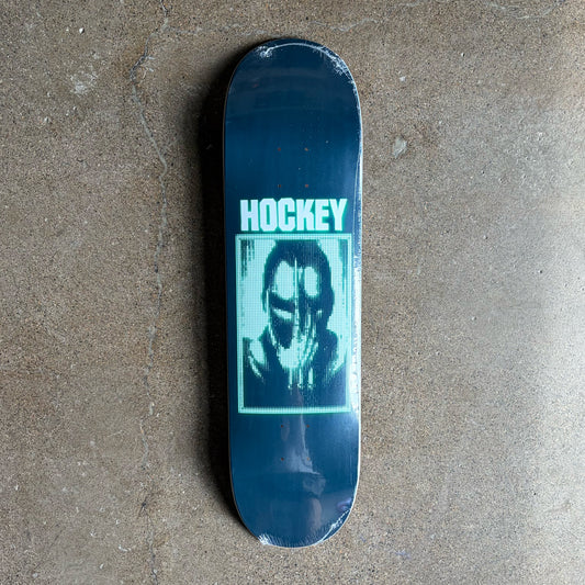 A dark blue hockey-themed skateboard deck with a graphic of a masked figure and the word 'HOCKEY' in light blue, photographed on a textured concrete floor.